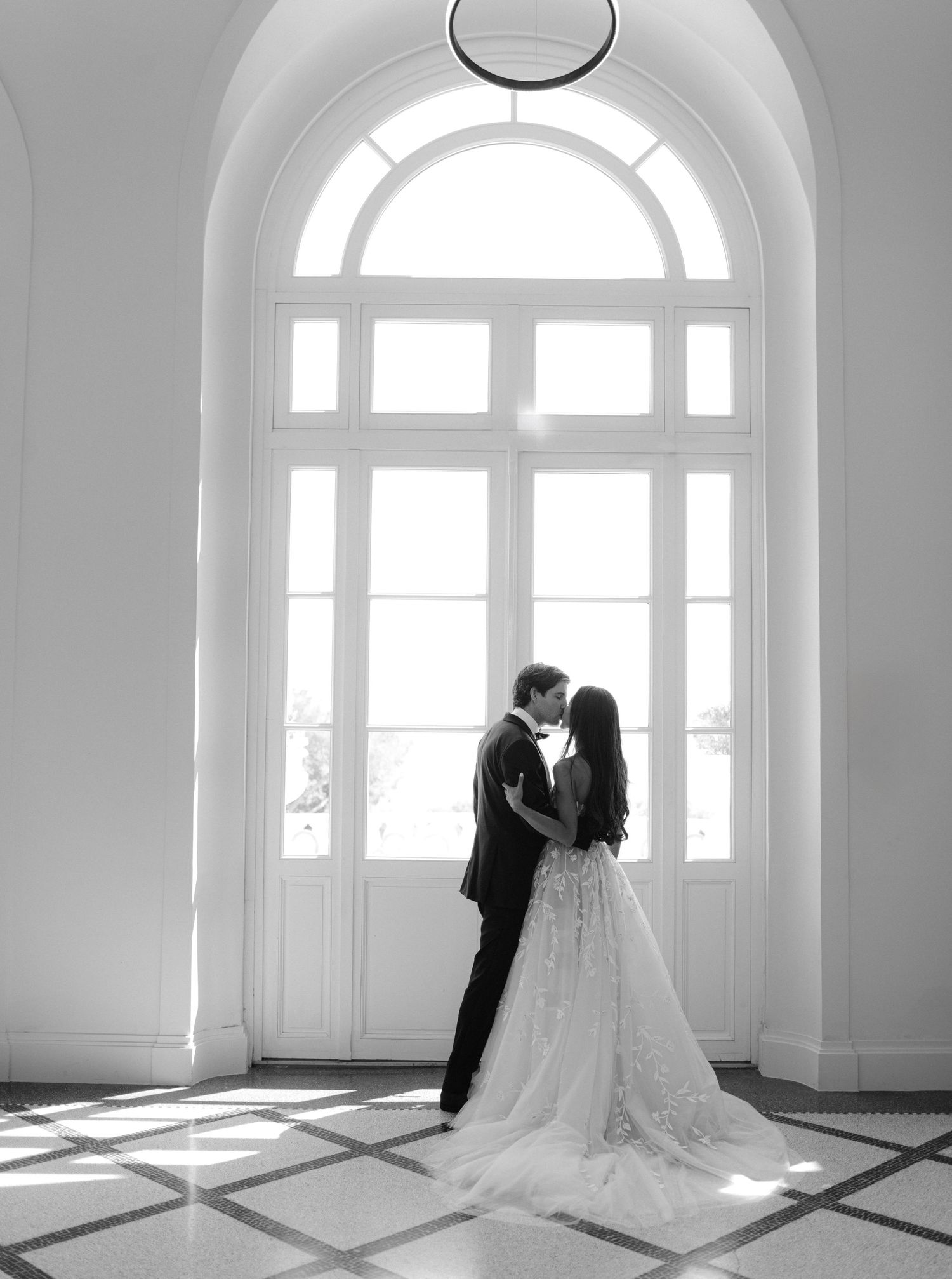 A series of five black and white wedding photographs showing an intimate dance and embrace in a sunlit room with arched windows.