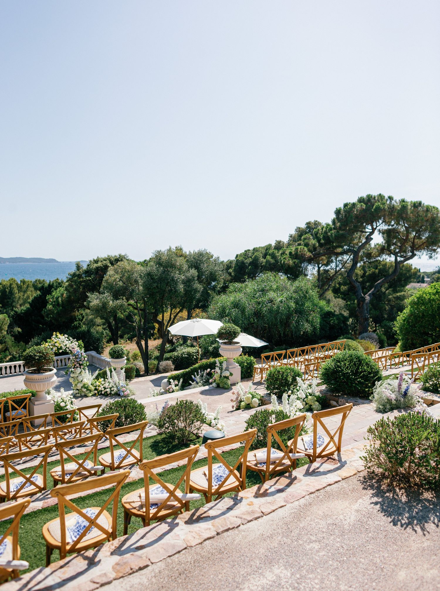 Wooden ceremony benches with floral arrangements line a scenic outdoor garden path overlooking a coastal landscape.