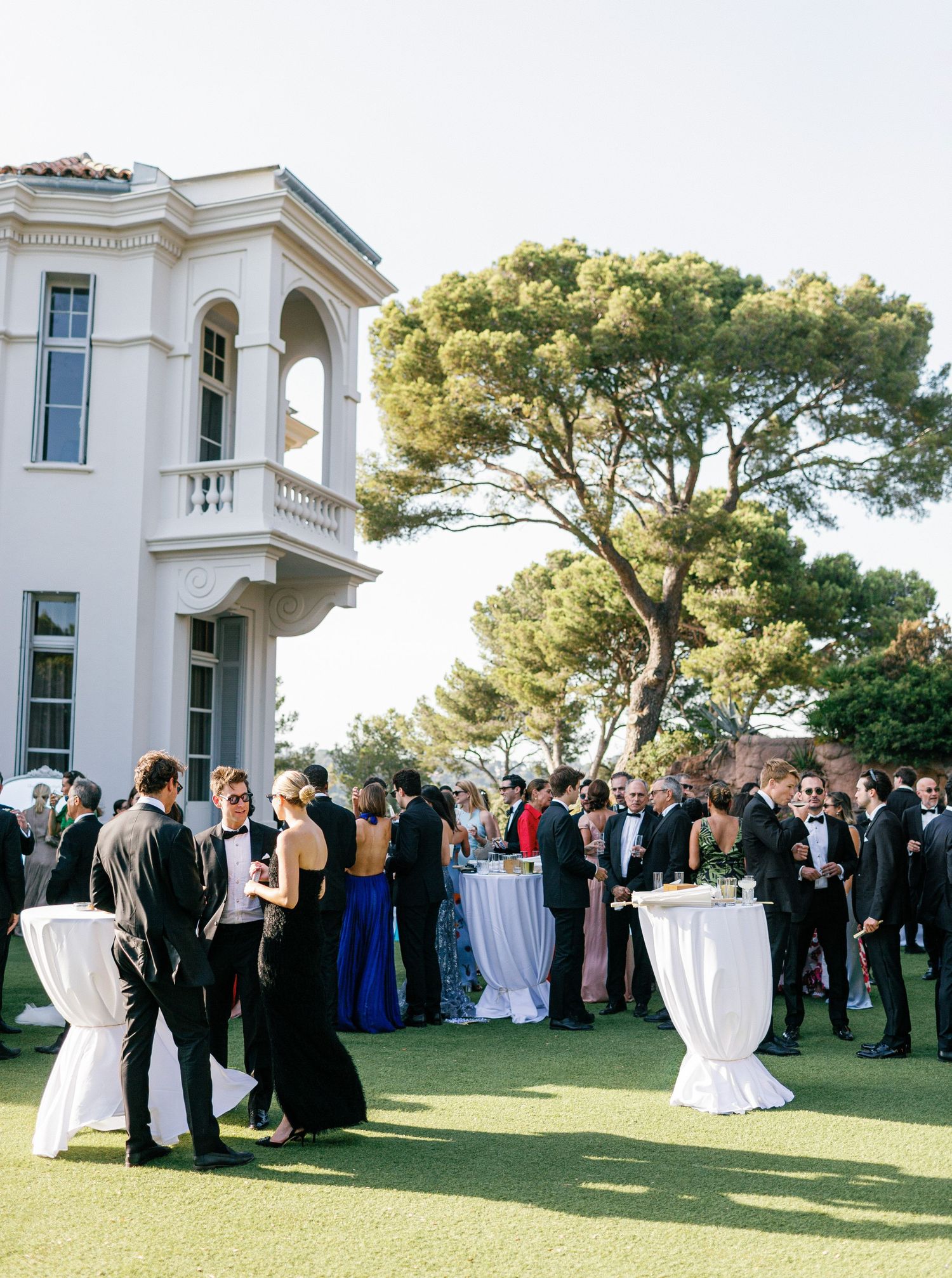Elegant outdoor wedding cocktail reception with guests mingling around white cocktail tables on a manicured lawn.