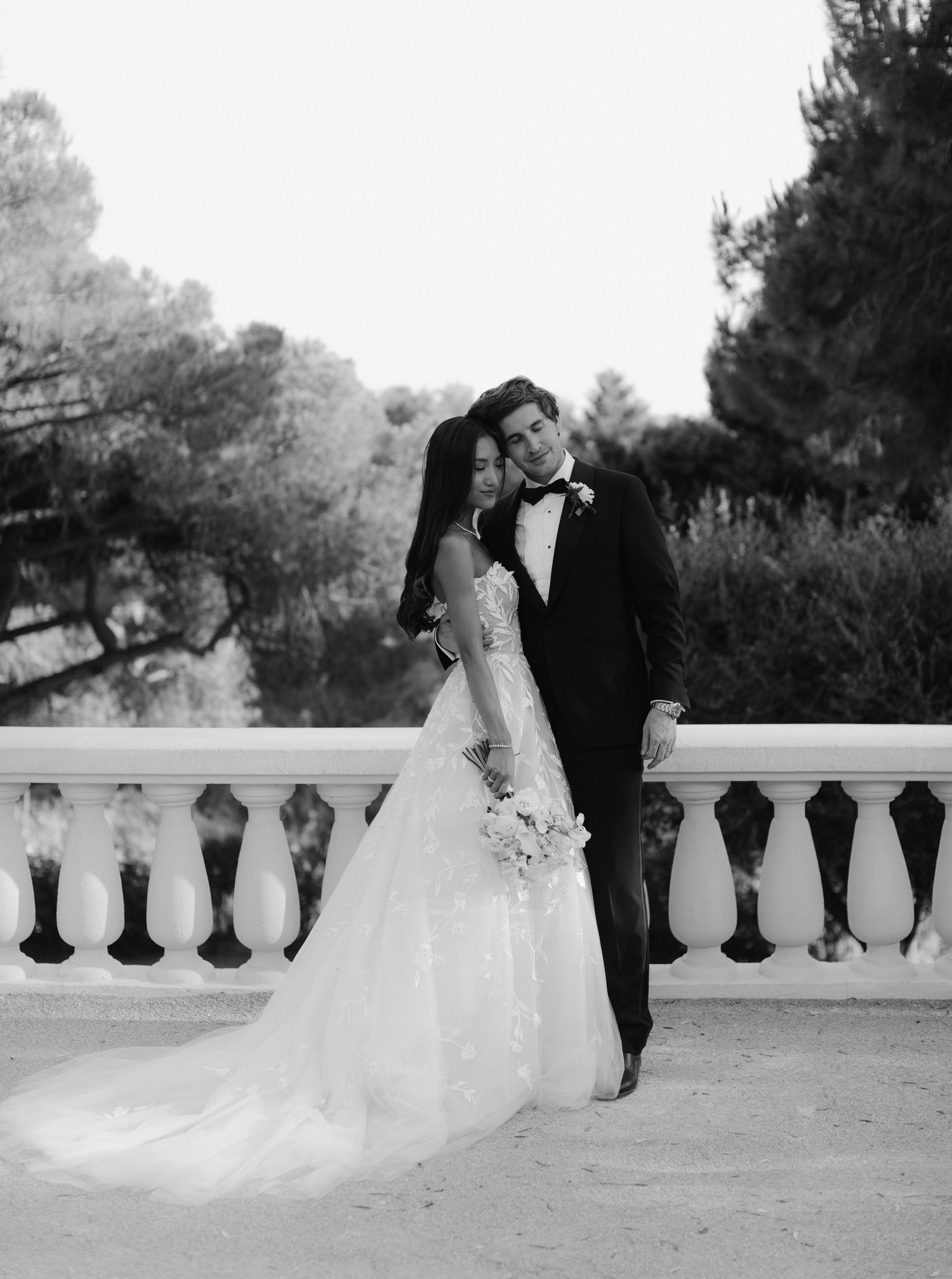 Romantic black and white wedding photo showing a couple embracing on an elegant outdoor terrace with stone balustrades at Castel Bay, Hyères