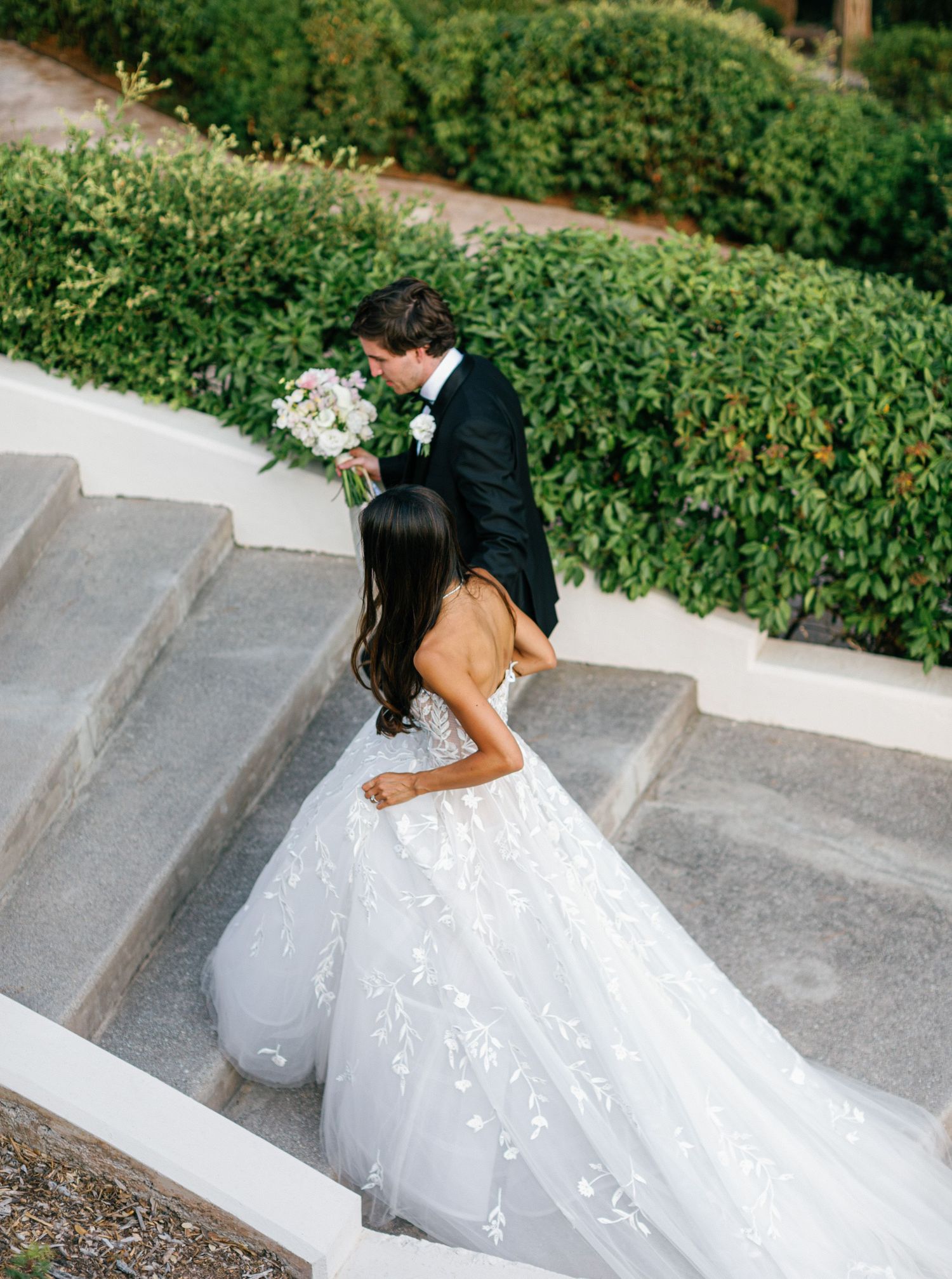 A romantic wedding photo showing a couple in formal attire embracing on outdoor garden steps.