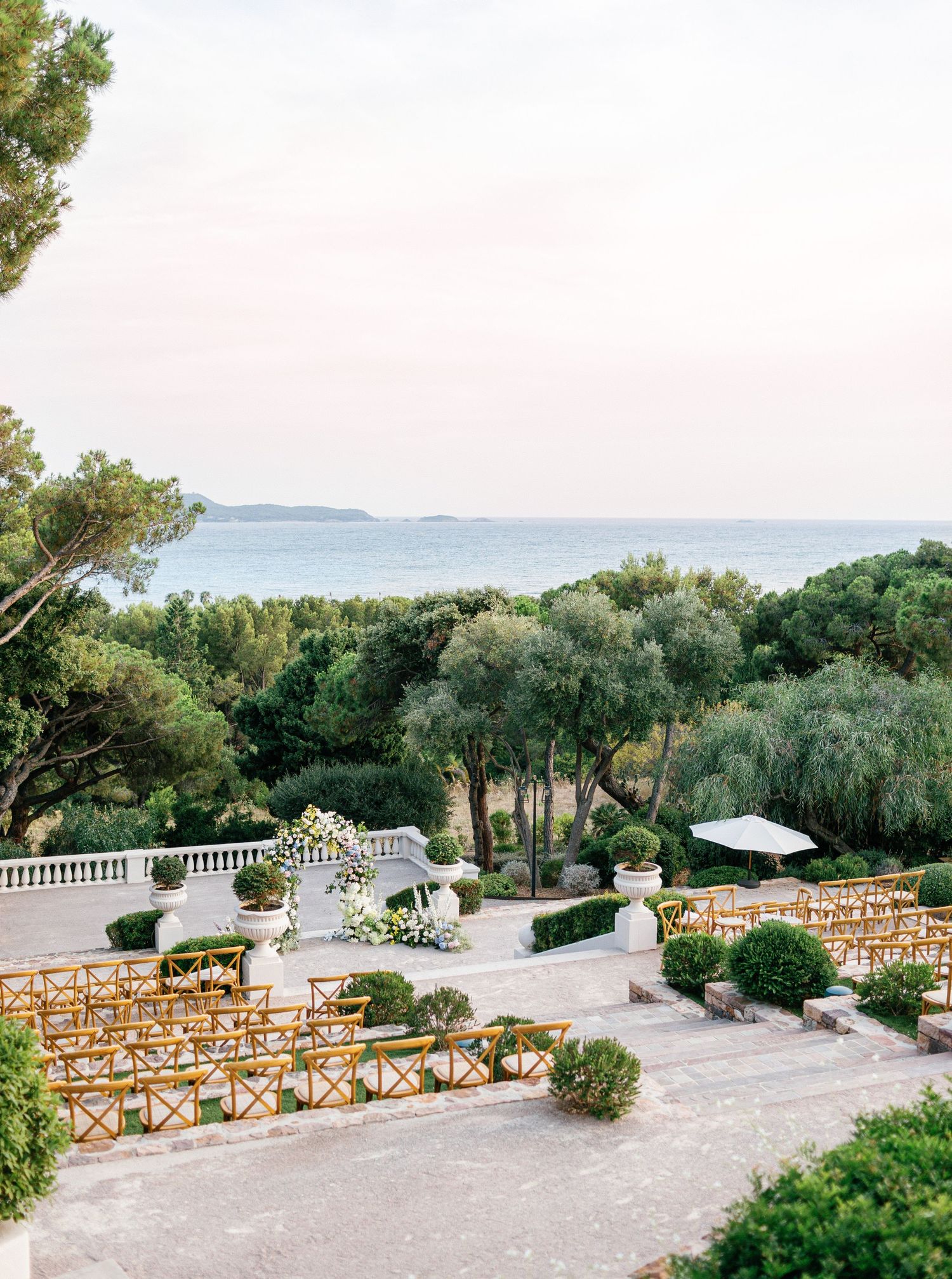 Outdoor wedding ceremony setup overlooking the sea with rows of wooden chairs arranged on a stone paved terrace.