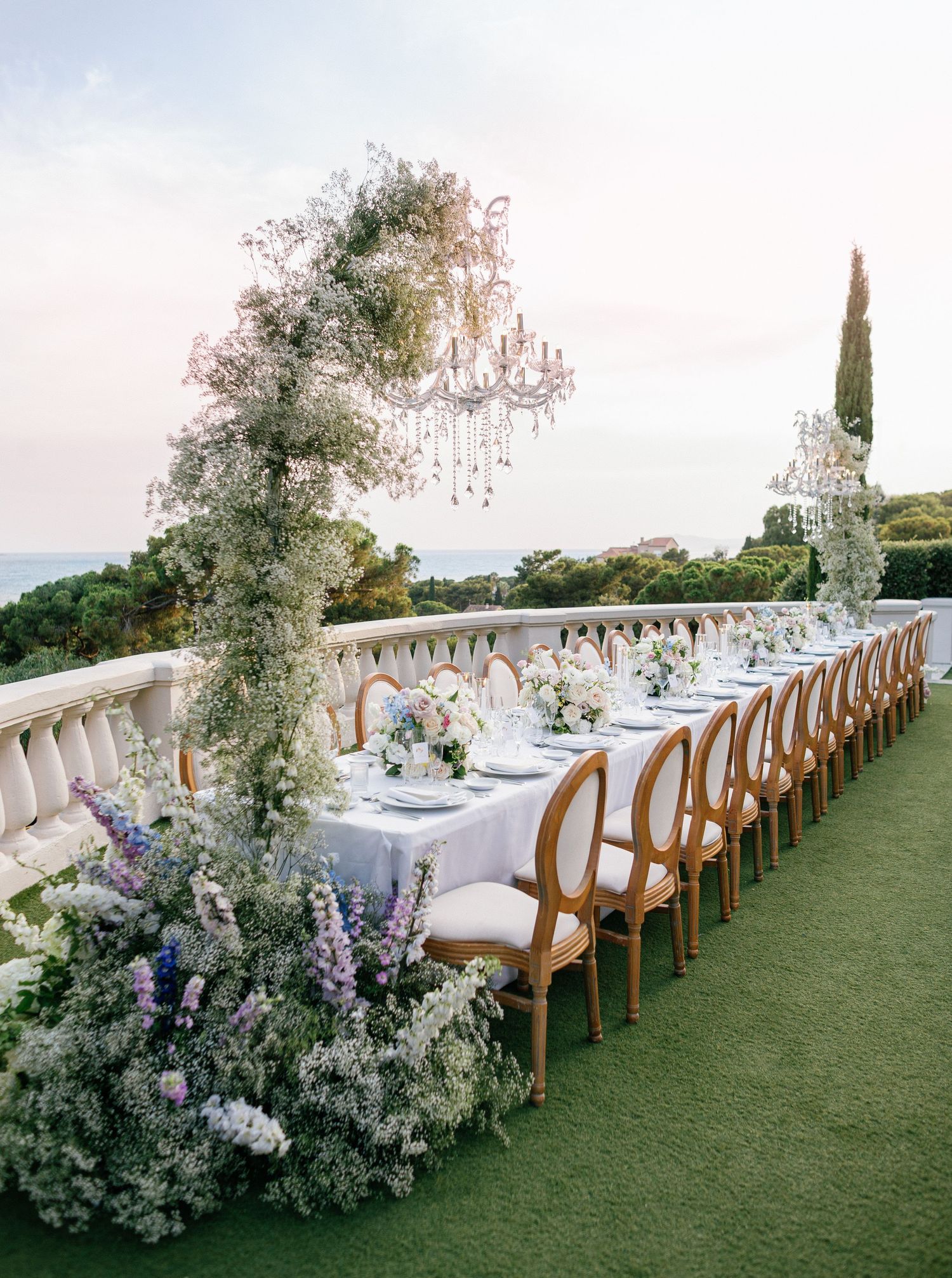 Elegant outdoor wedding reception setup with long dining tables decorated with white linens and floral arrangements at Castel Bay, Hyères.