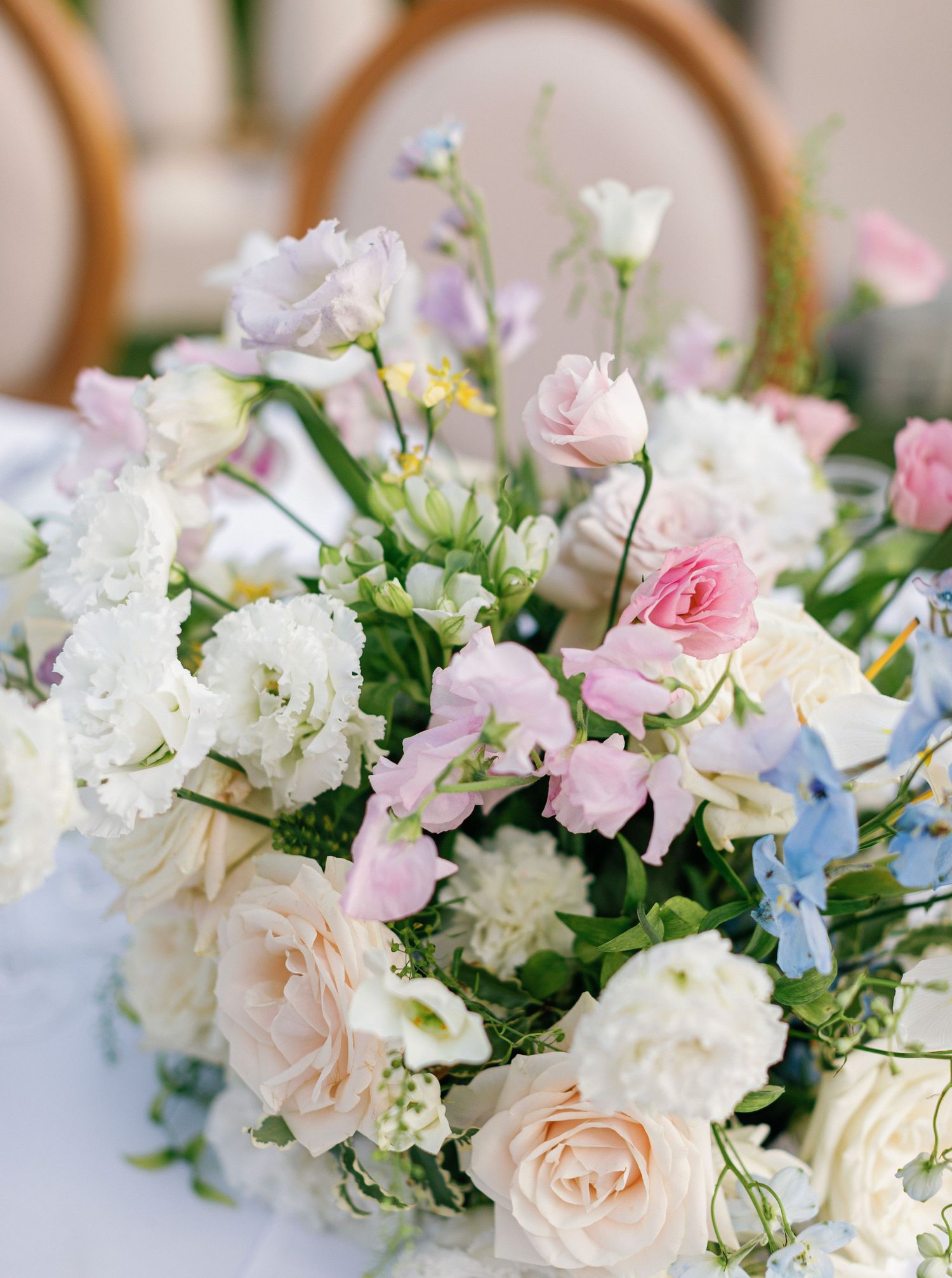 Delicate wedding bouquet featuring soft pink roses, white carnations, and light blue flowers with fresh greenery.