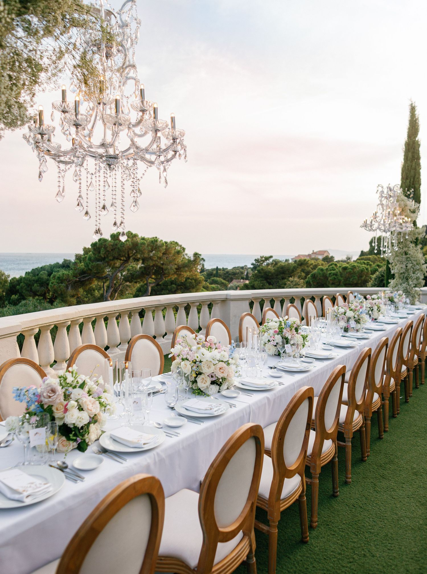 Elegant outdoor wedding reception table setup with crystal chandelier and ocean view featuring white linens and blush florals.
