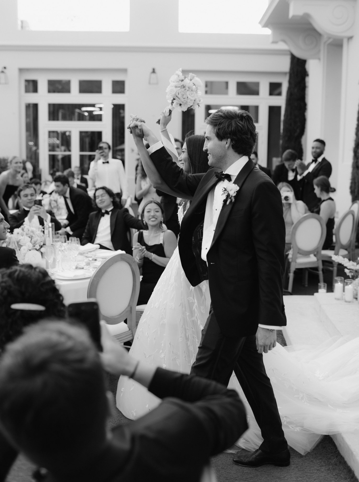 Black and white photo showing wedding guests and newlyweds walking in and celebrating at Castel Bay, Hyères, French Riviera.
