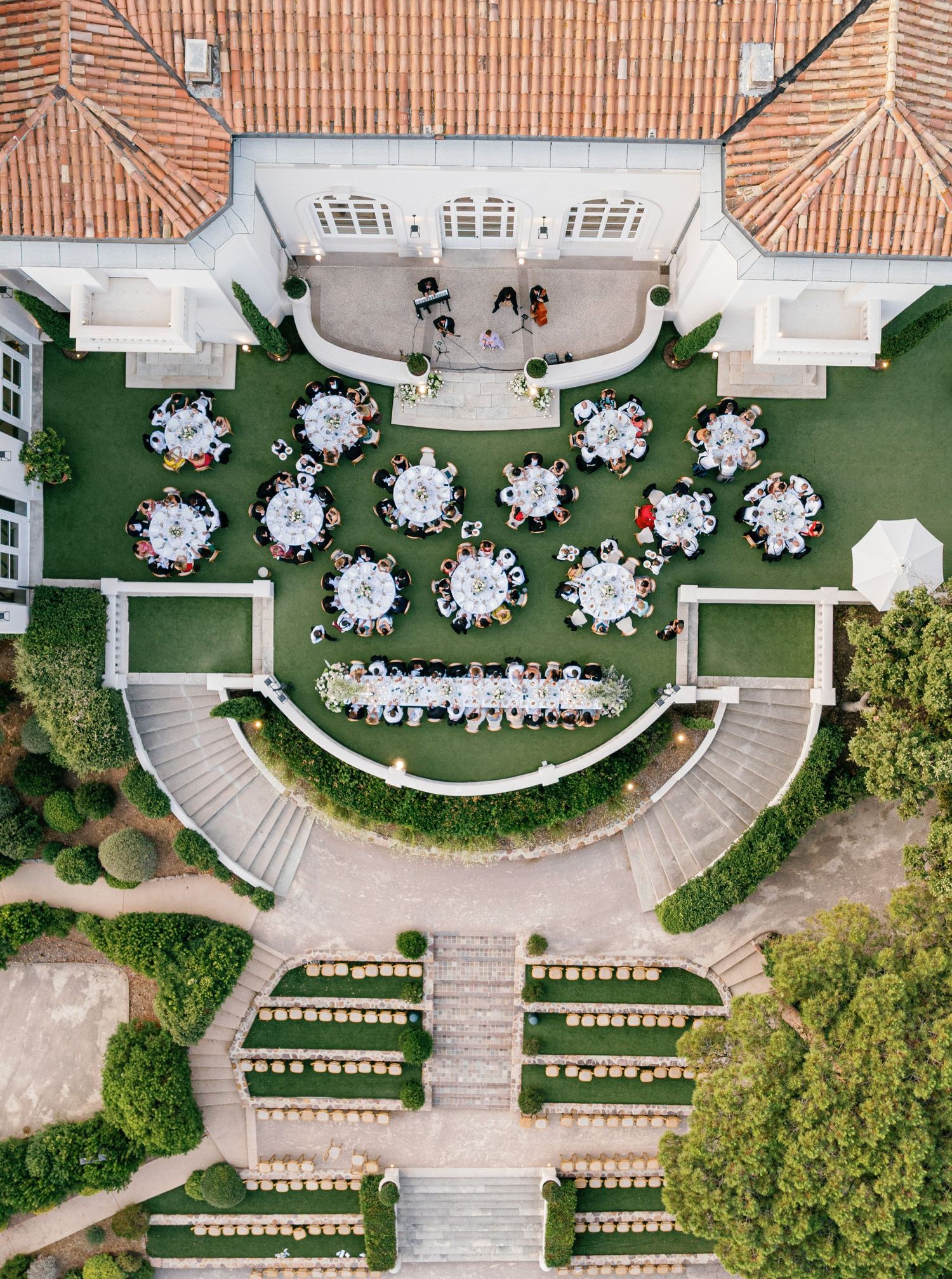 Aerial view of an elegant outdoor wedding reception with round tables arranged on a manicured lawn next to a Castel Bay, Hyères.