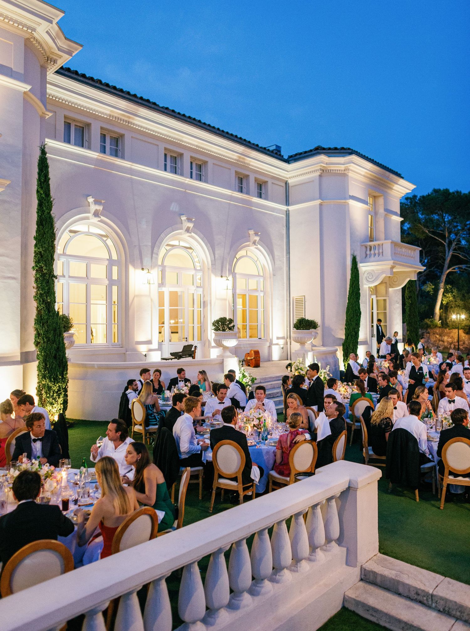 Elegant outdoor wedding reception at dusk with white columned terrace and formal dining setup illuminated by warm lights at Castel Bay.
