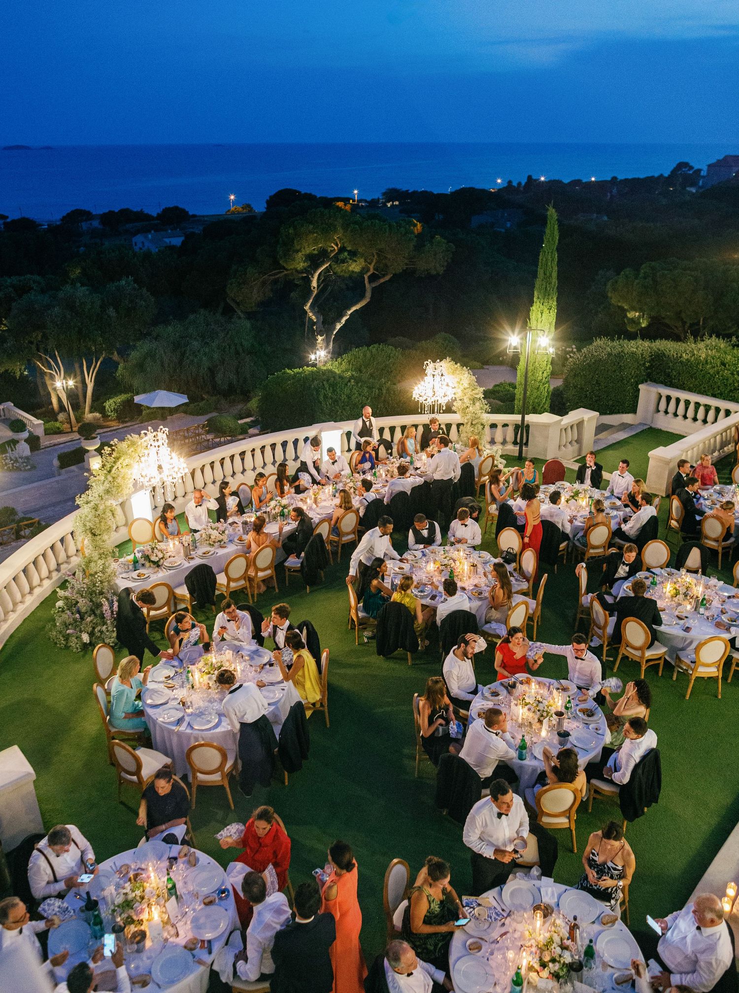 Elegant outdoor wedding reception dinner setup with glowing string lights and tables arranged on a garden lawn at dusk.