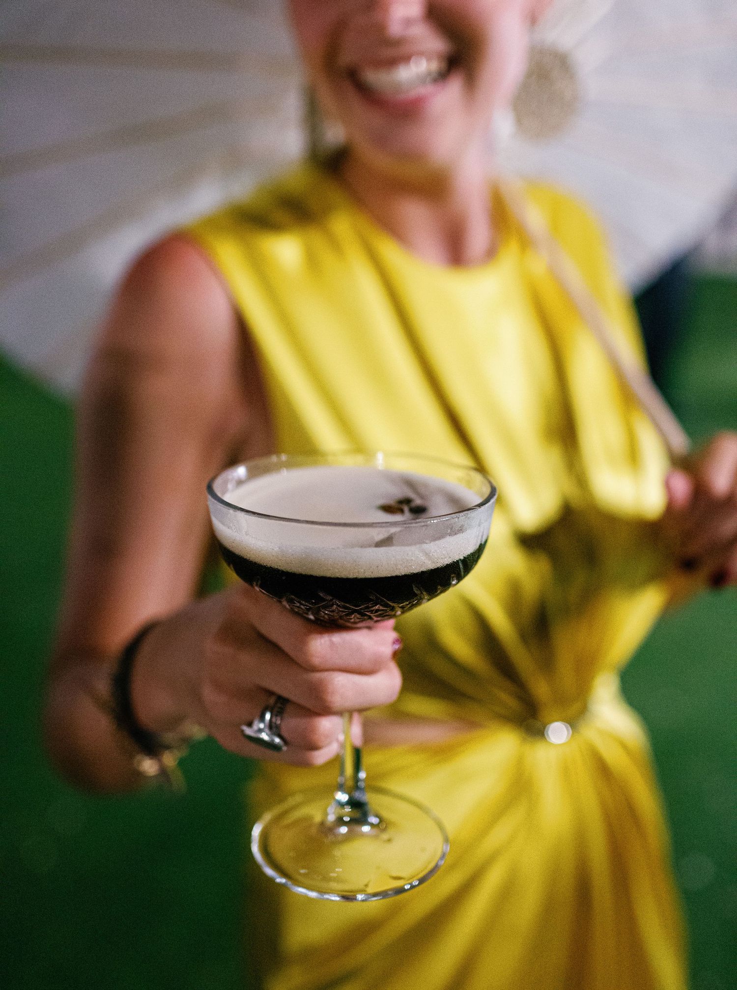A sequence showing an espresso martini cocktail in a stemmed glass held by someone wearing a yellow dress.