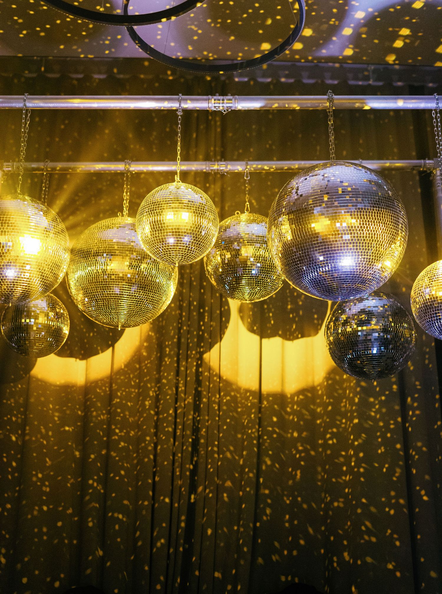 Glittering disco balls hanging from ceiling with golden lights creating a magical party atmosphere in sequence of shots.
