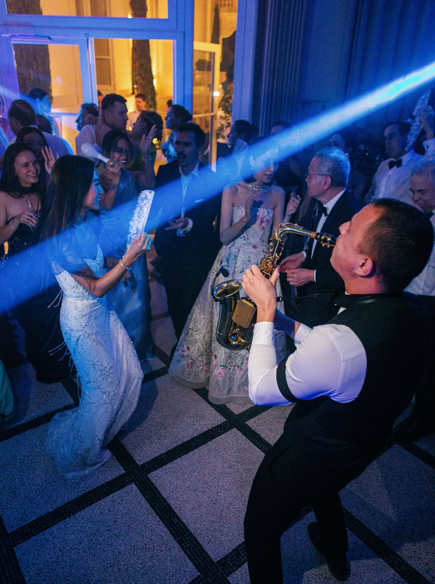 Dancing wedding guests enjoying a lively celebration with blue spotlights illuminating their synchronized moves on the dance floor.