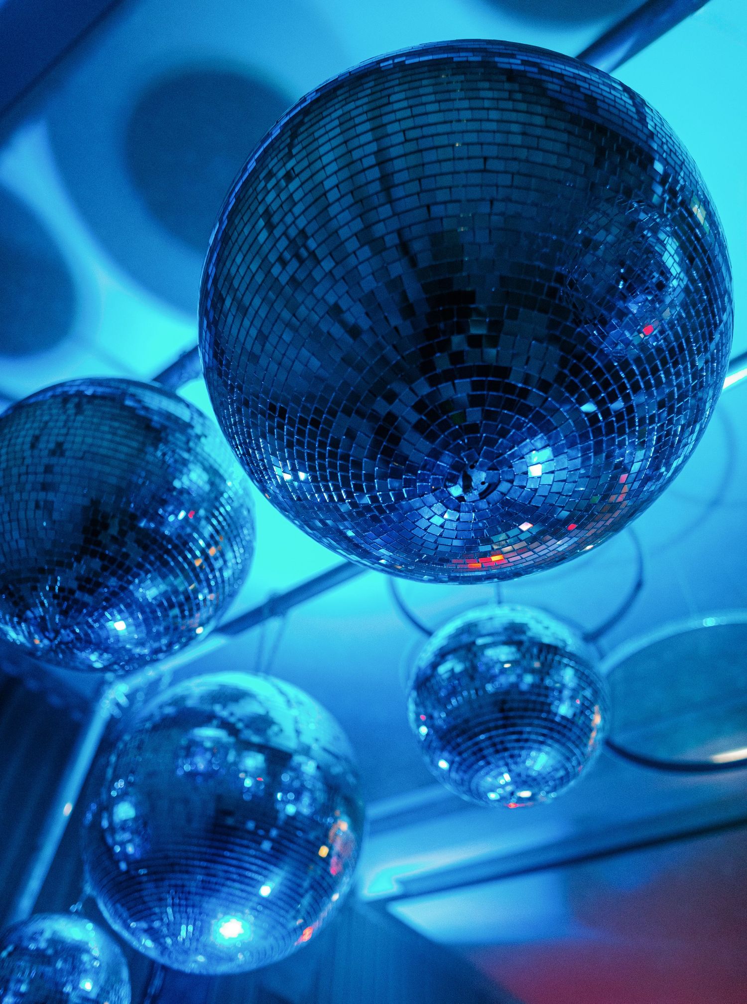 Multiple shiny disco balls hanging from ceiling reflect blue lighting in a nightclub or party atmosphere.