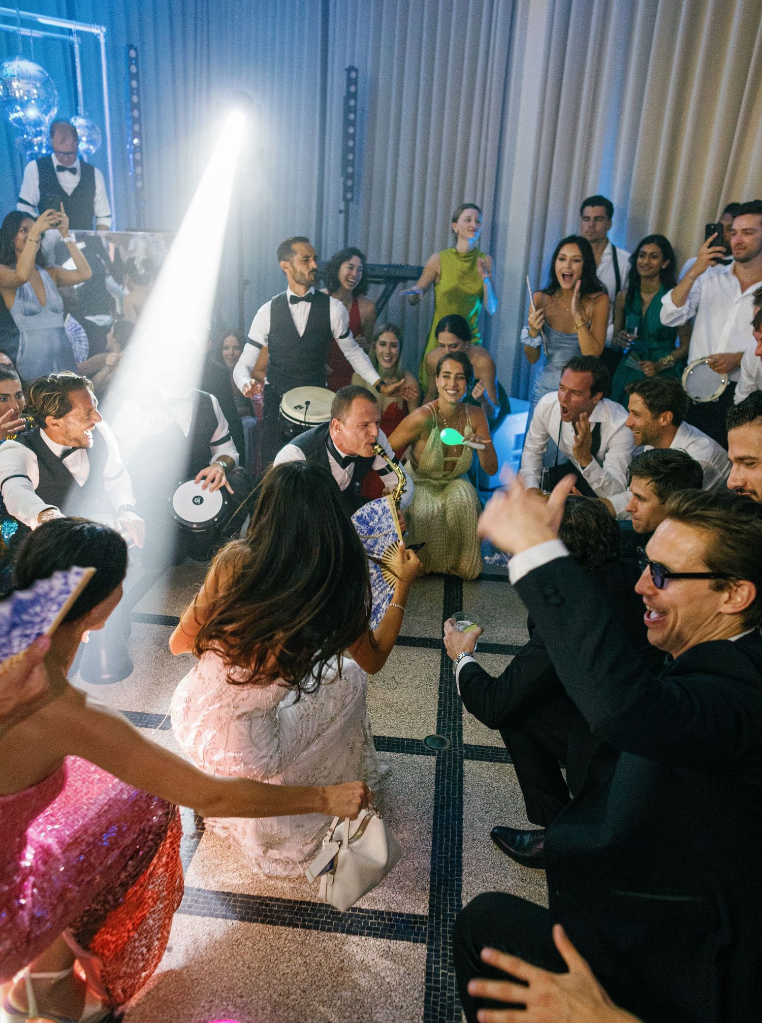 Wedding guests dancing and having fun on a crowded dance floor at a reception celebration with blue lighting.