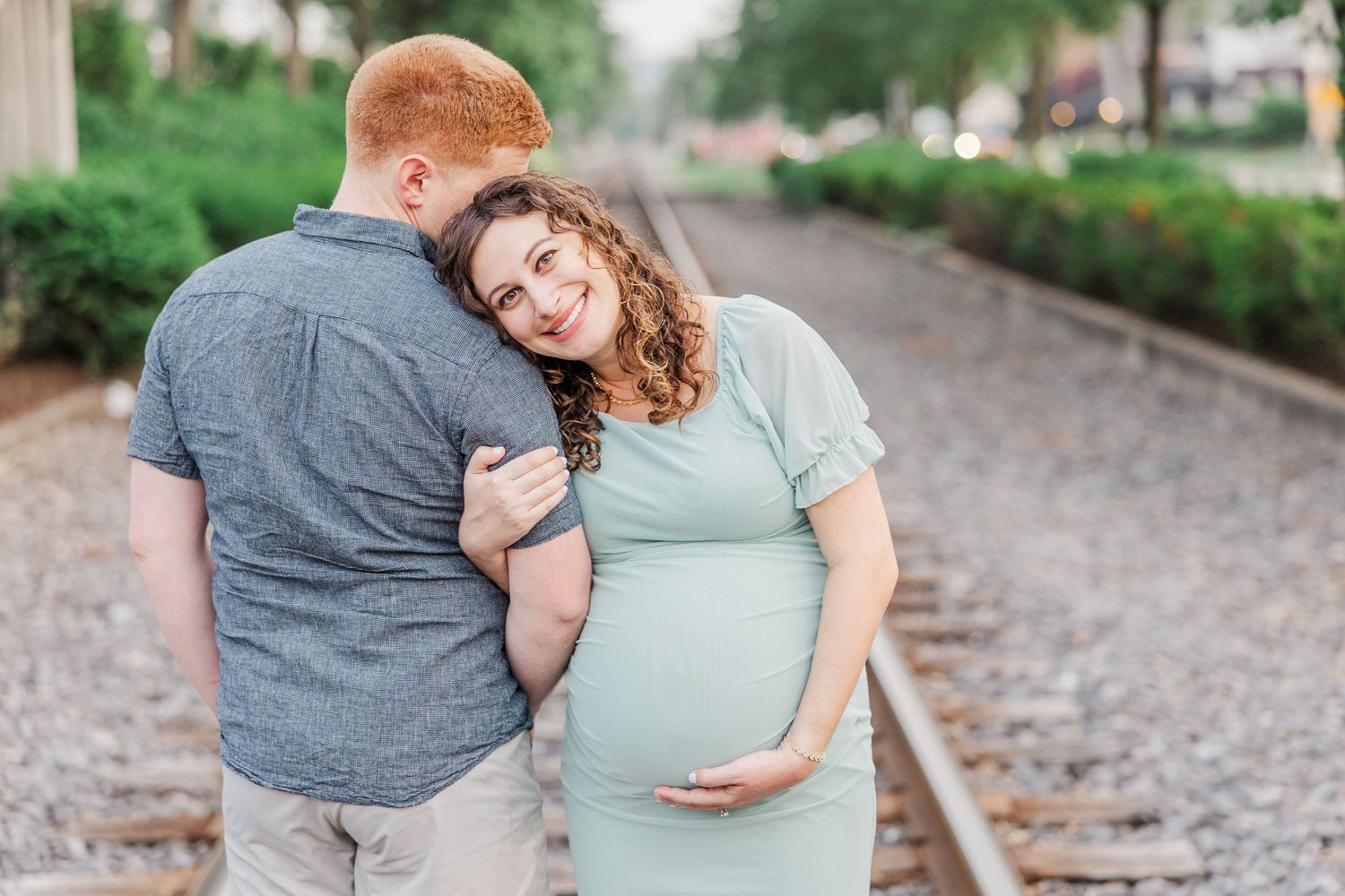 A romantic maternity photoshoot on train tracks with soft natural lighting.