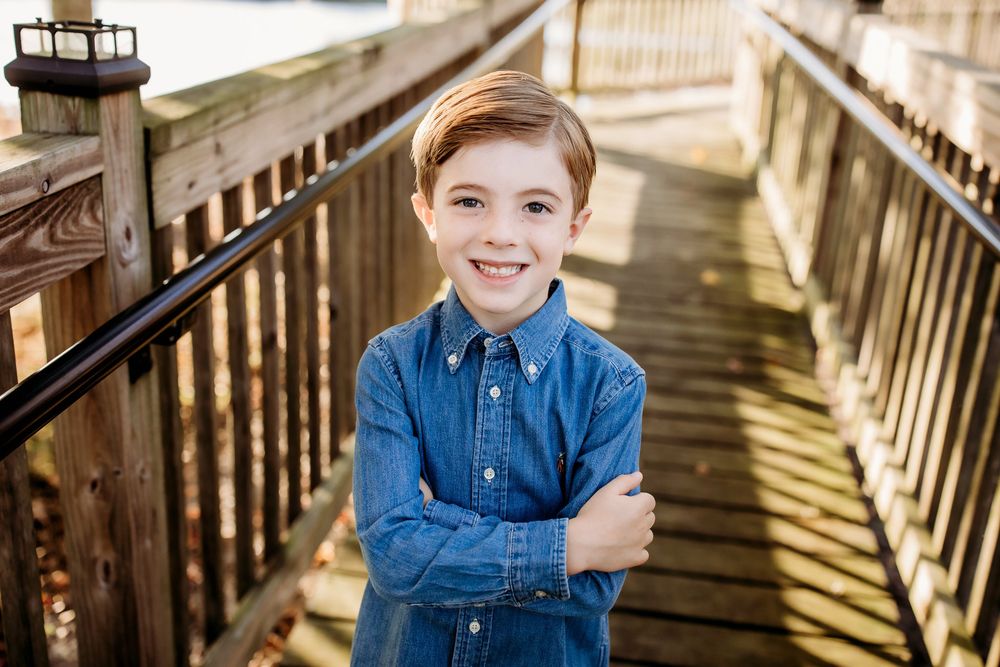Child in denim shirt sitting on wooden stairs with natural lighting and rustic backdrop.