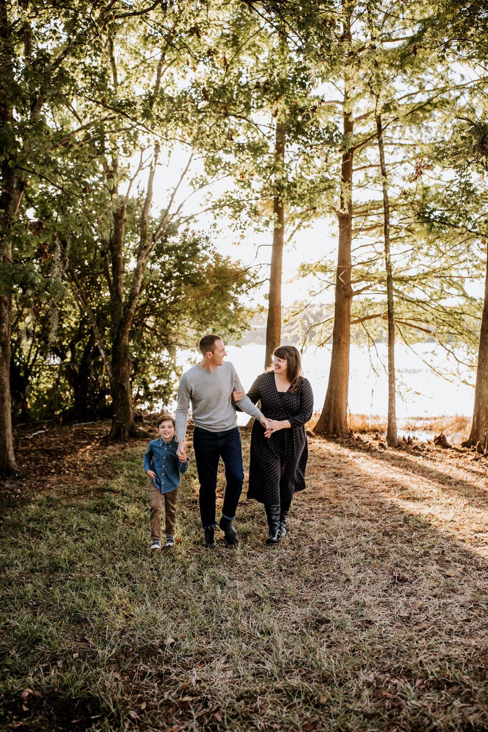 Family walks together through sunlit forest path casting long shadows among tall pine trees in autumn.