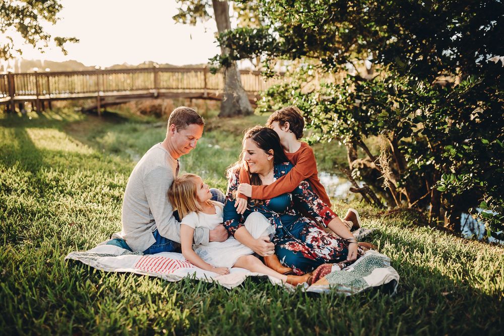 Family enjoys intimate sunset picnic on blanket in golden sunlit meadow during golden hour photography session.