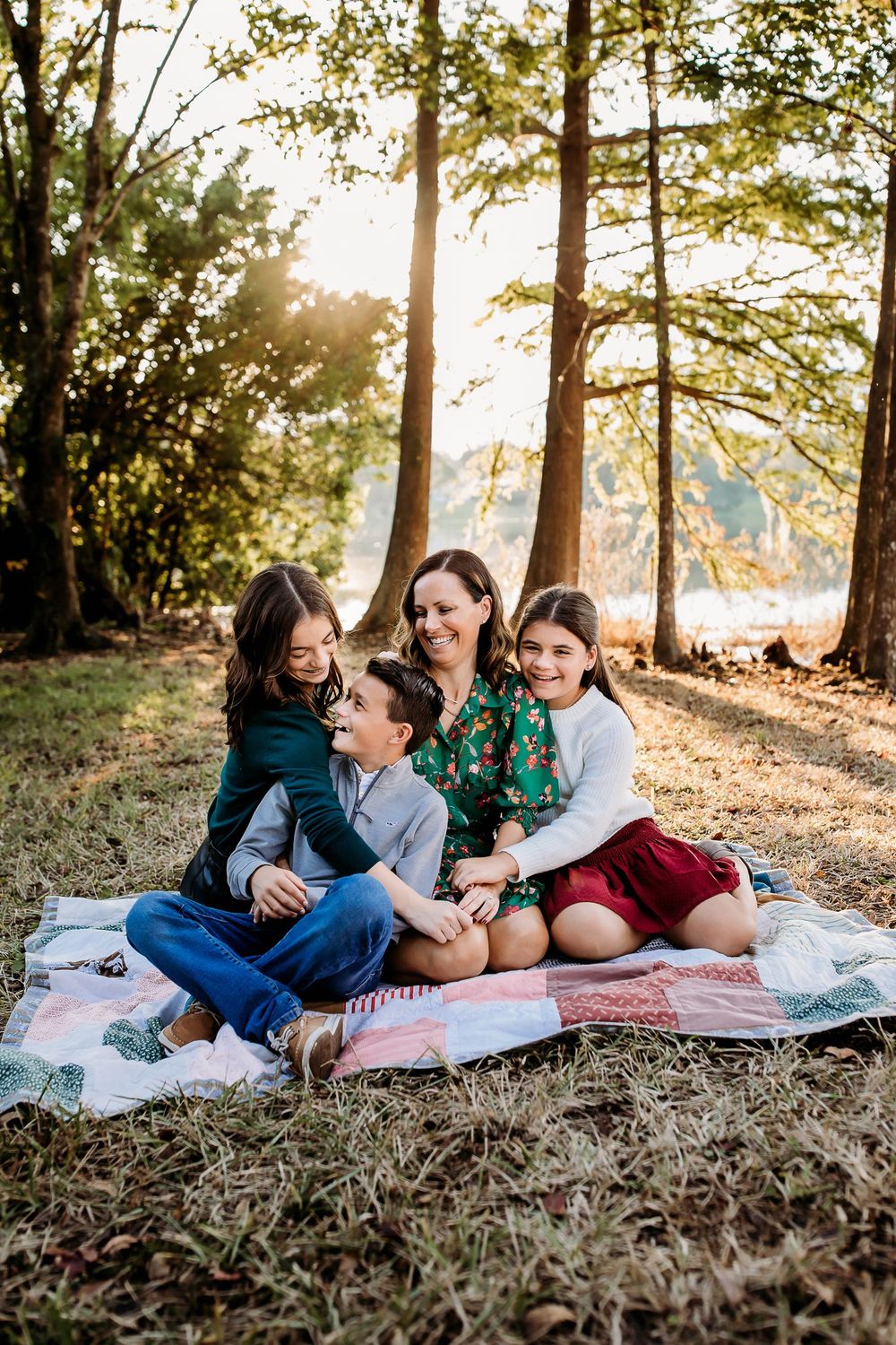 A family relaxes together on blankets in a sunny forest setting during golden hour lighting.