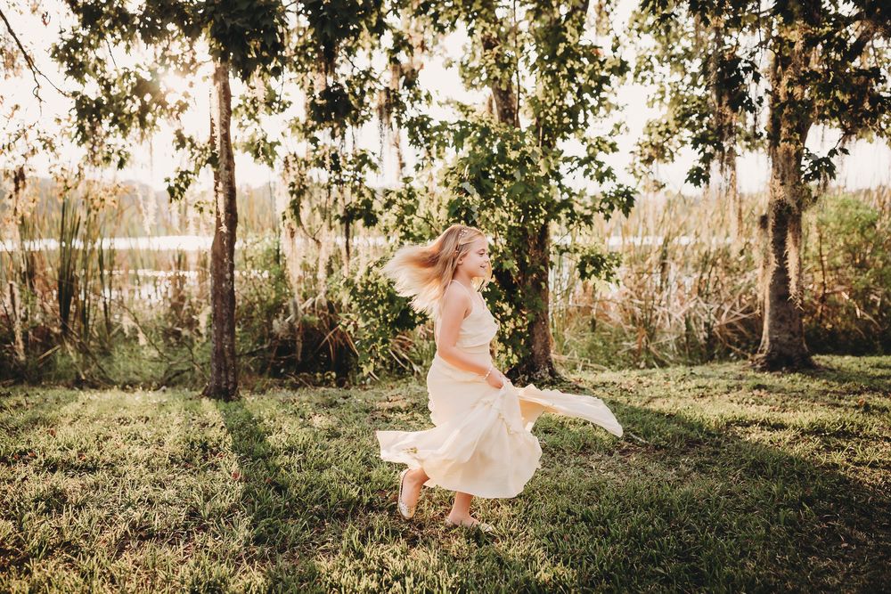 Woman in white dress skips gracefully through a sunlit grove of trees during a warm autumn day.