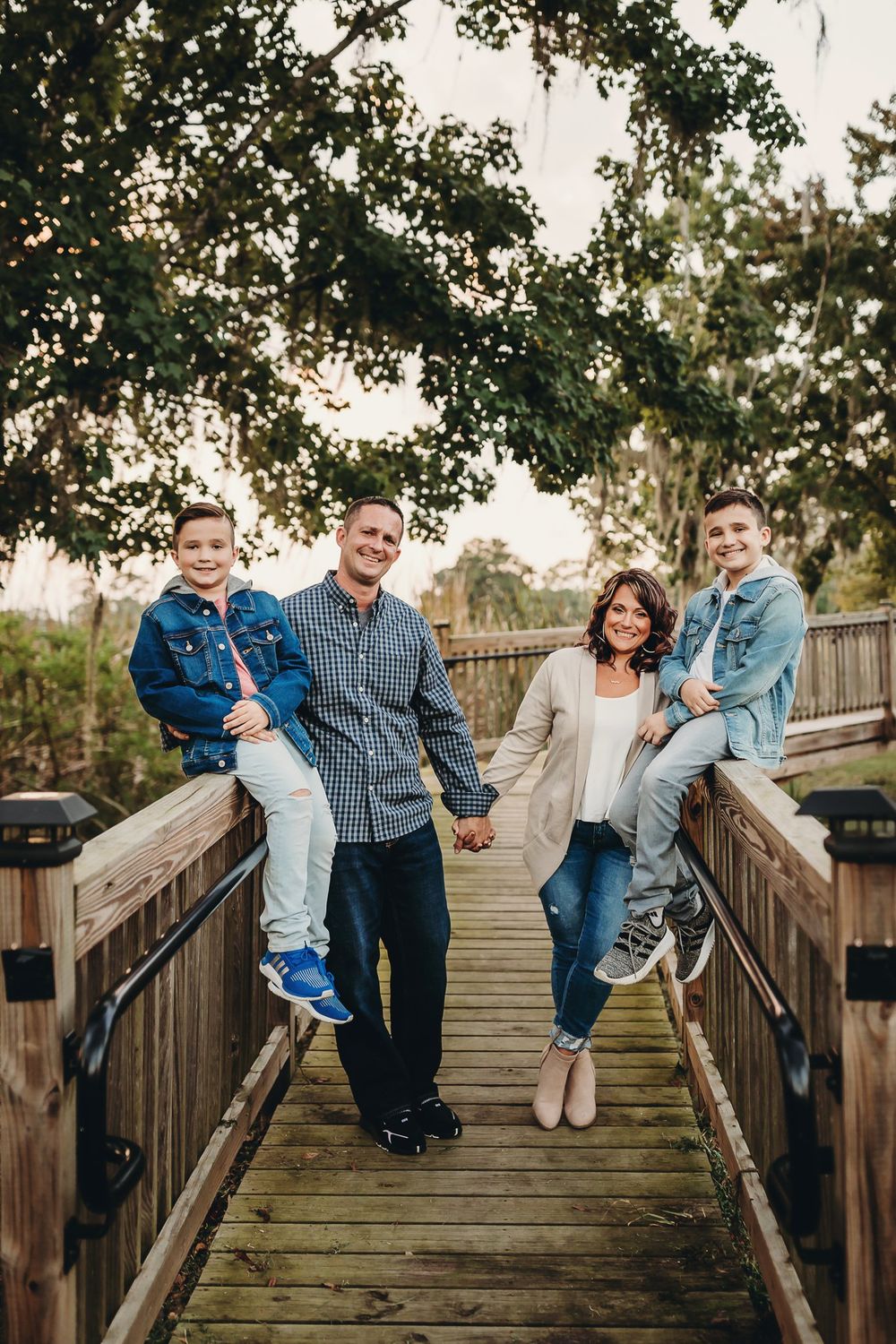 A family poses playfully on a wooden boardwalk surrounded by trees during an outdoor photo session.