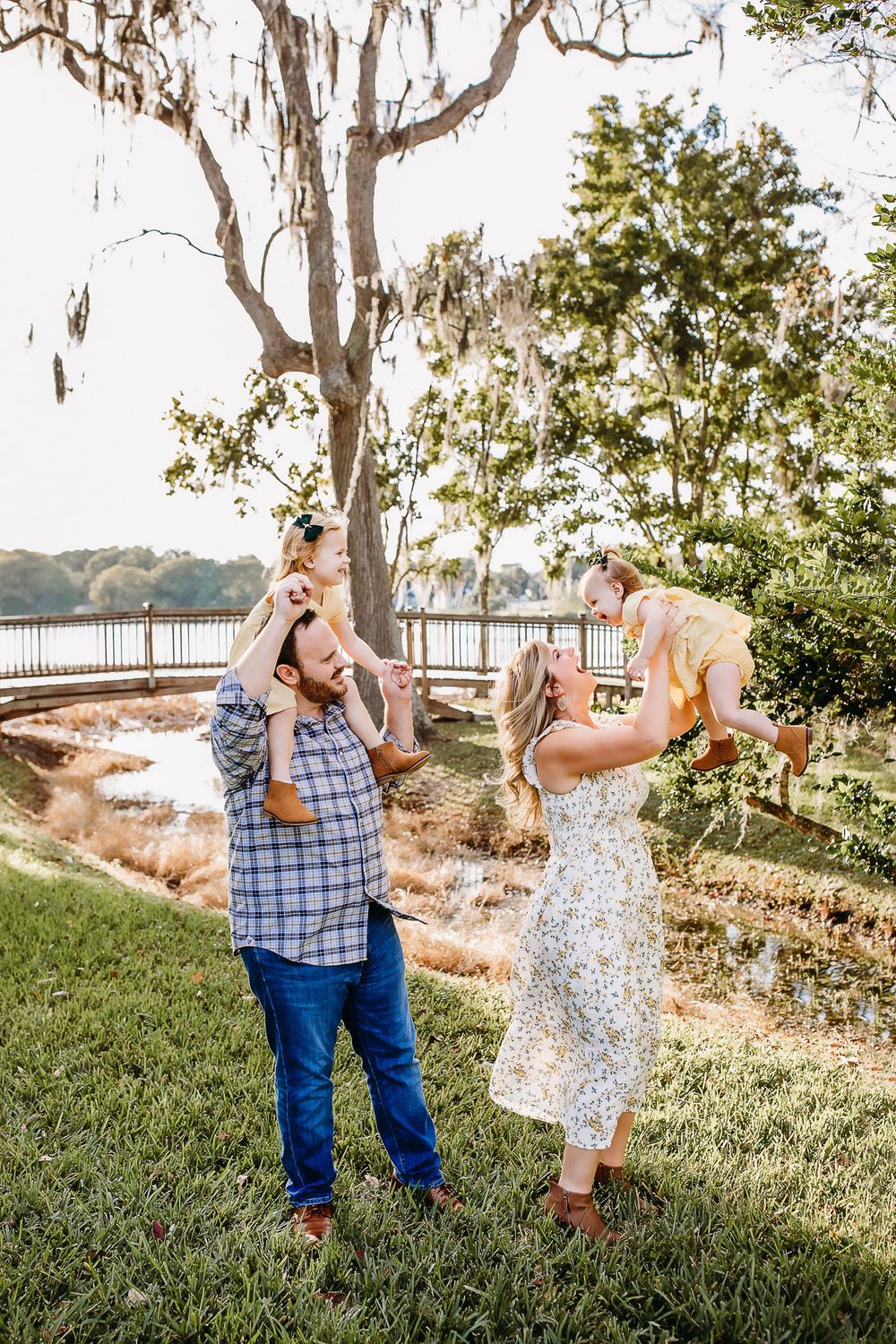 A couple shares a playful moment together outdoors on a grassy hill with Spanish moss covered trees in the background.