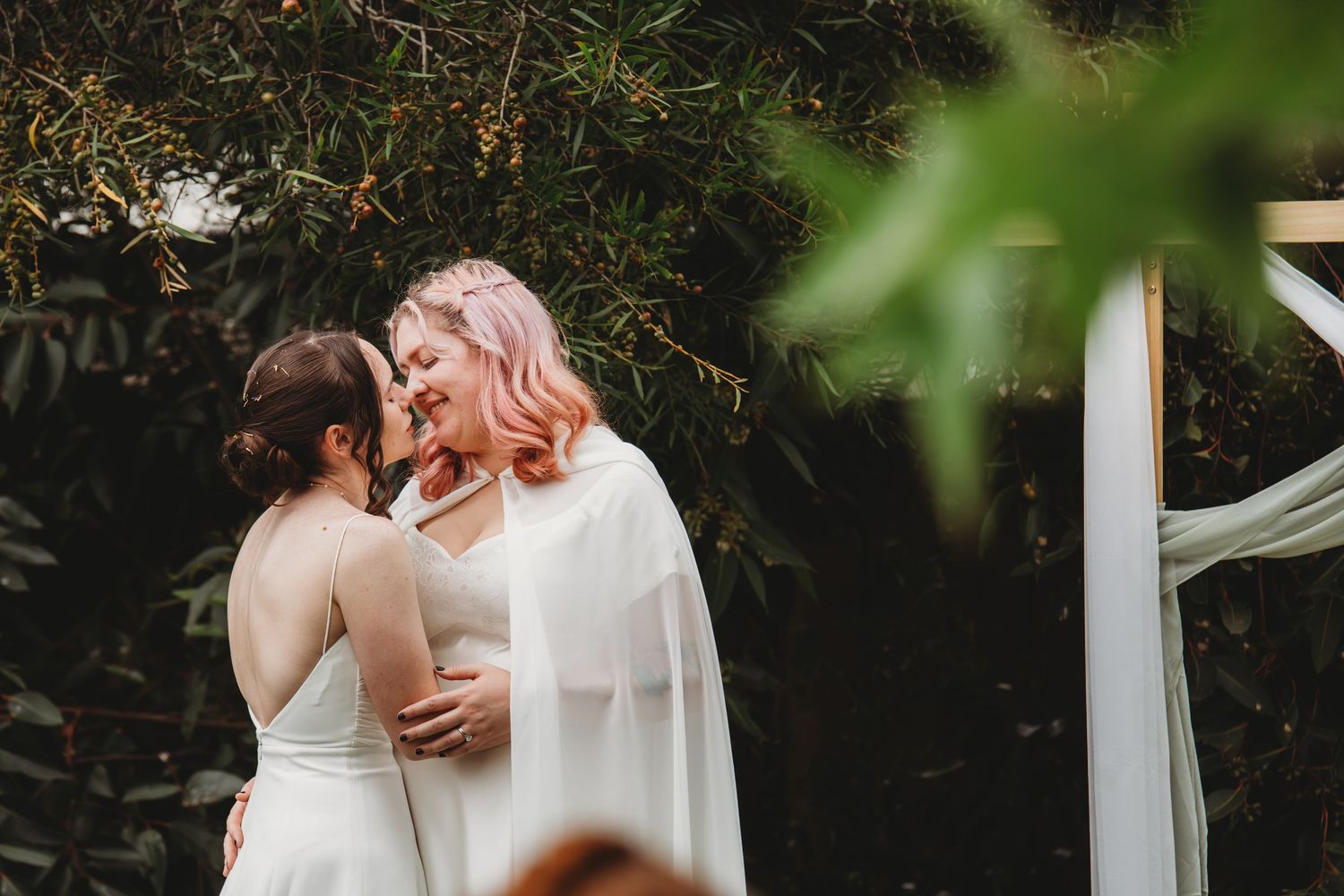 A couple embraces tenderly during a romantic outdoor wedding ceremony surrounded by greenery and sunlight.