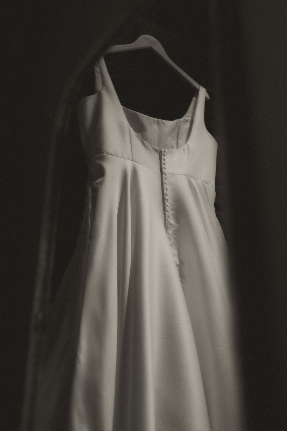 White vintage sleeveless dress with button details hangs gracefully against a dark background.