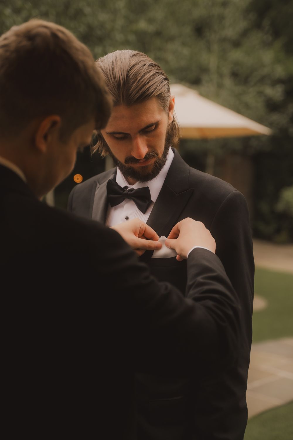 A groomsman helps adjust another's bowtie in a series of candid wedding preparation photos outdoors.