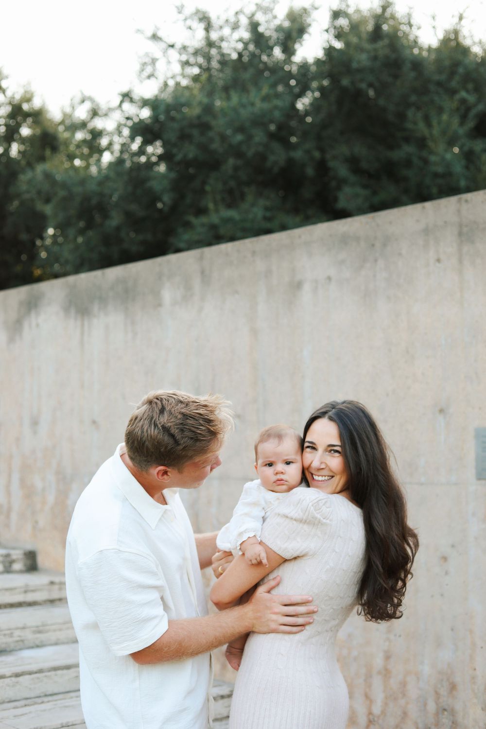 Candid family photography session against concrete wall with natural lighting.
