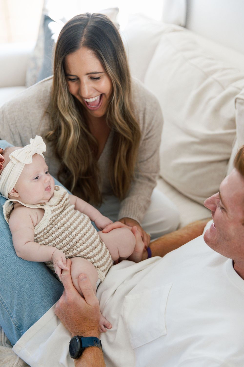 Natural lifestyle photos of parents sharing joyful moments with baby on white couch.