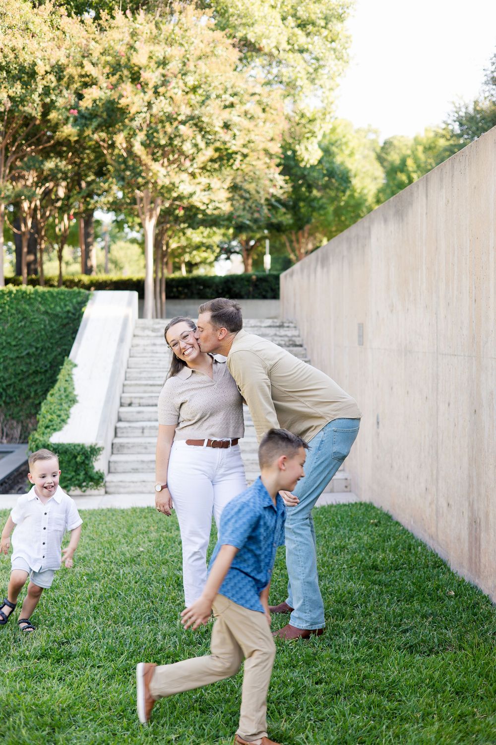 A family shares a playful moment on grass near concrete steps outdoors.