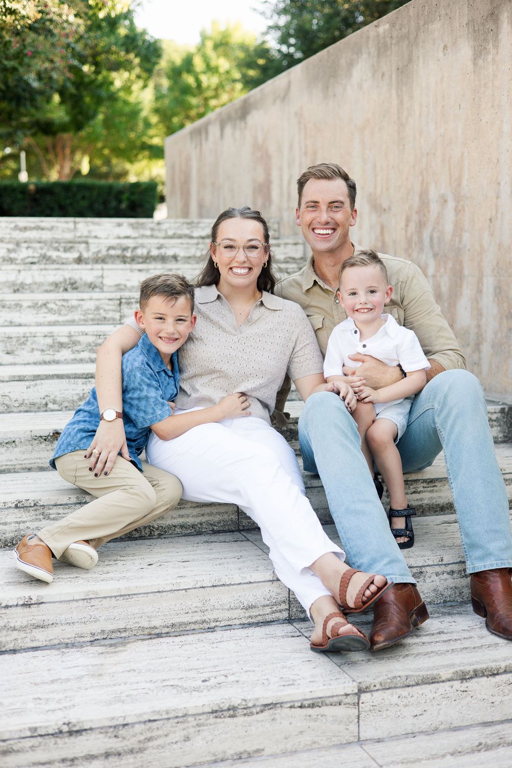 A family sits together casually on outdoor stone steps in coordinated outfits.