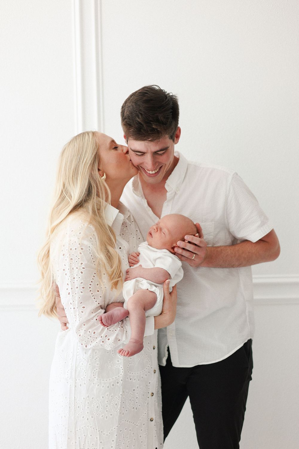 Family shares an intimate moment with their baby while wearing white against a bright backdrop.