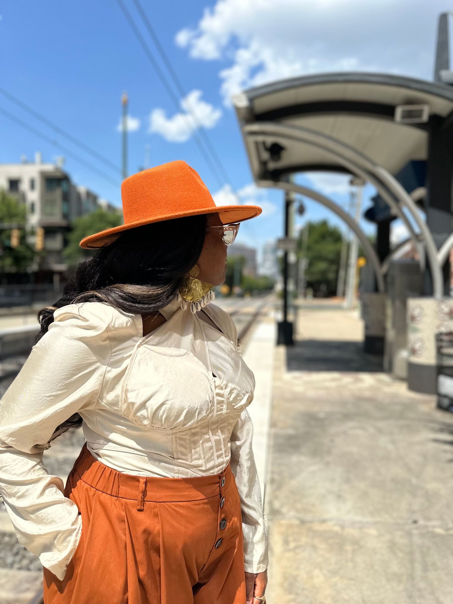 A person in a cream shirt and orange dress stands beside a concrete bridge structure under a bright blue sky.