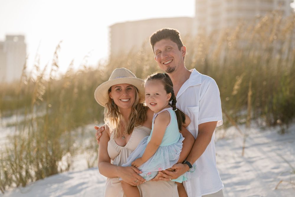 Family portrait session at sunset on white sand beach with sea oats and golden light.