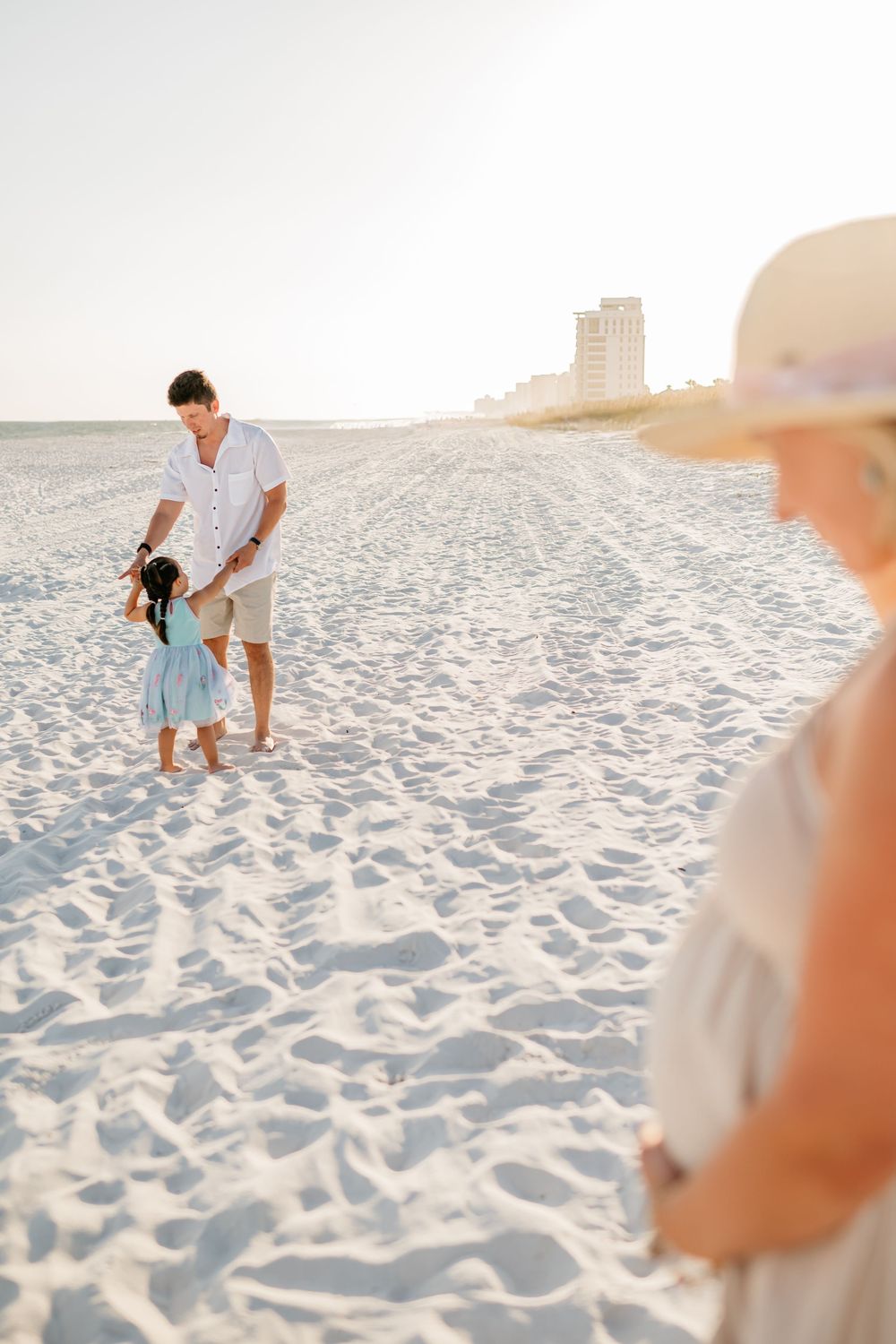 Family walking together on white sandy beach with high-rise buildings in background.