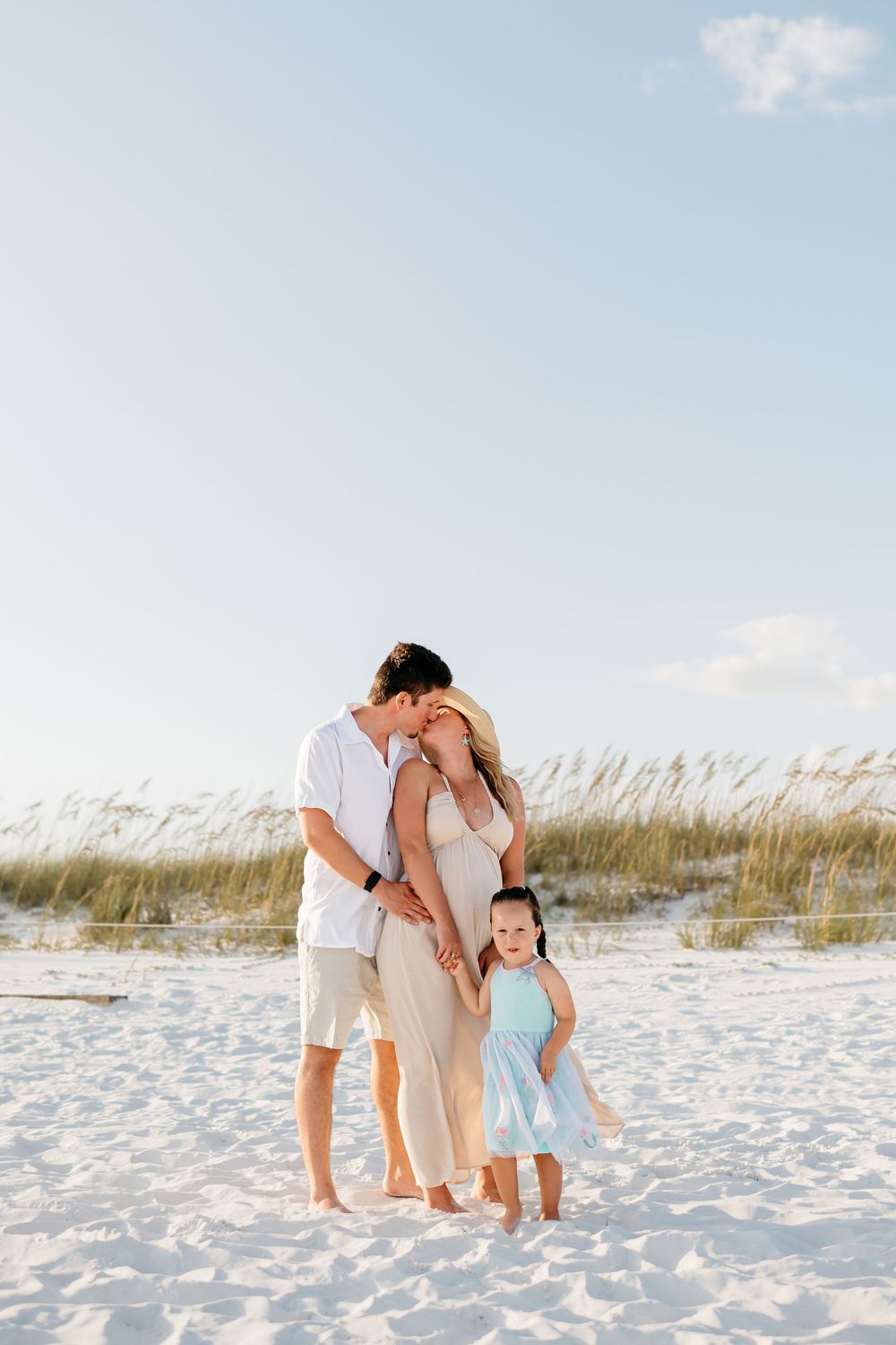 Family enjoying tender moments together while posing on pristine white sand beach at sunset.