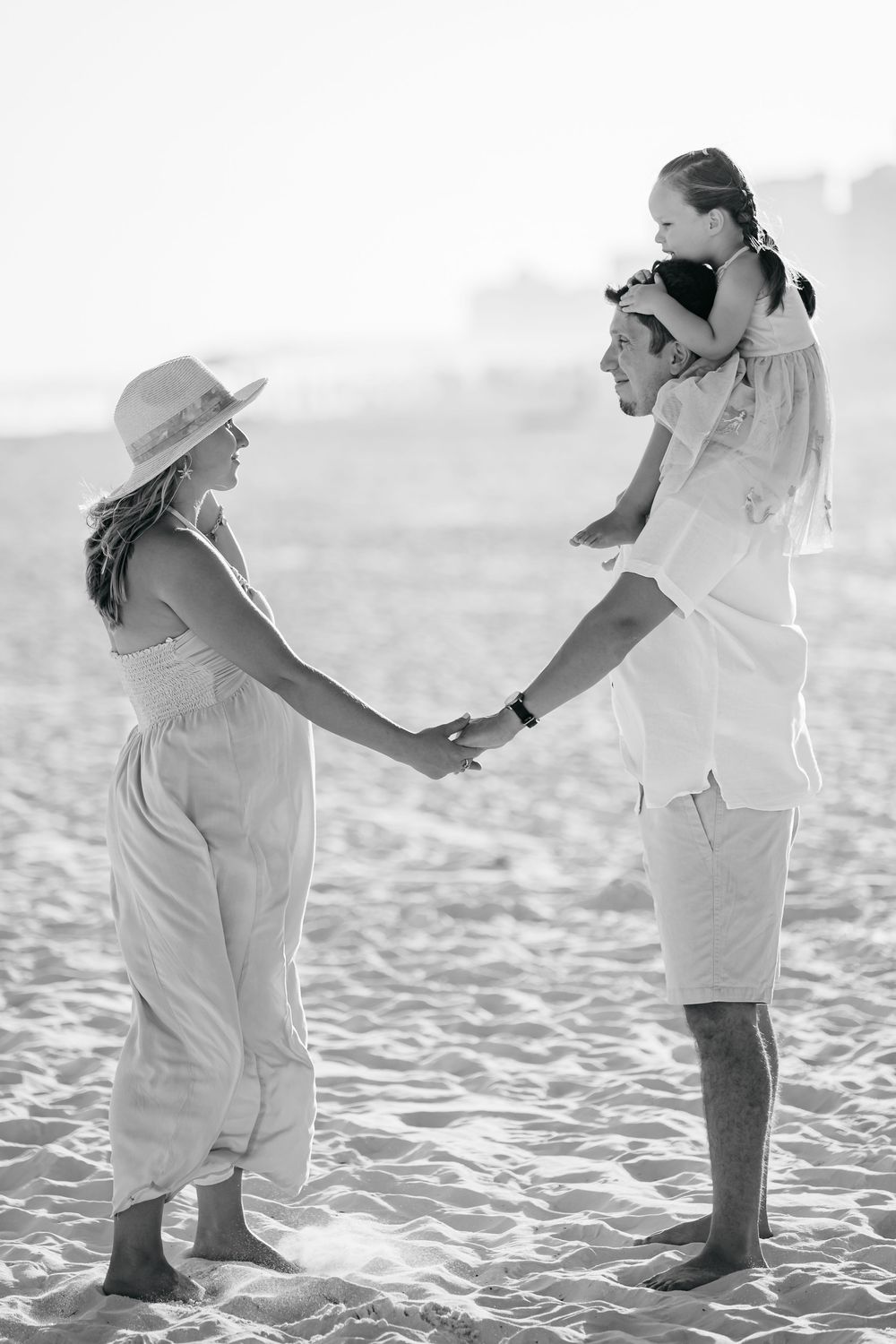 Black and white photo of family holding hands in a circle on beach sand.