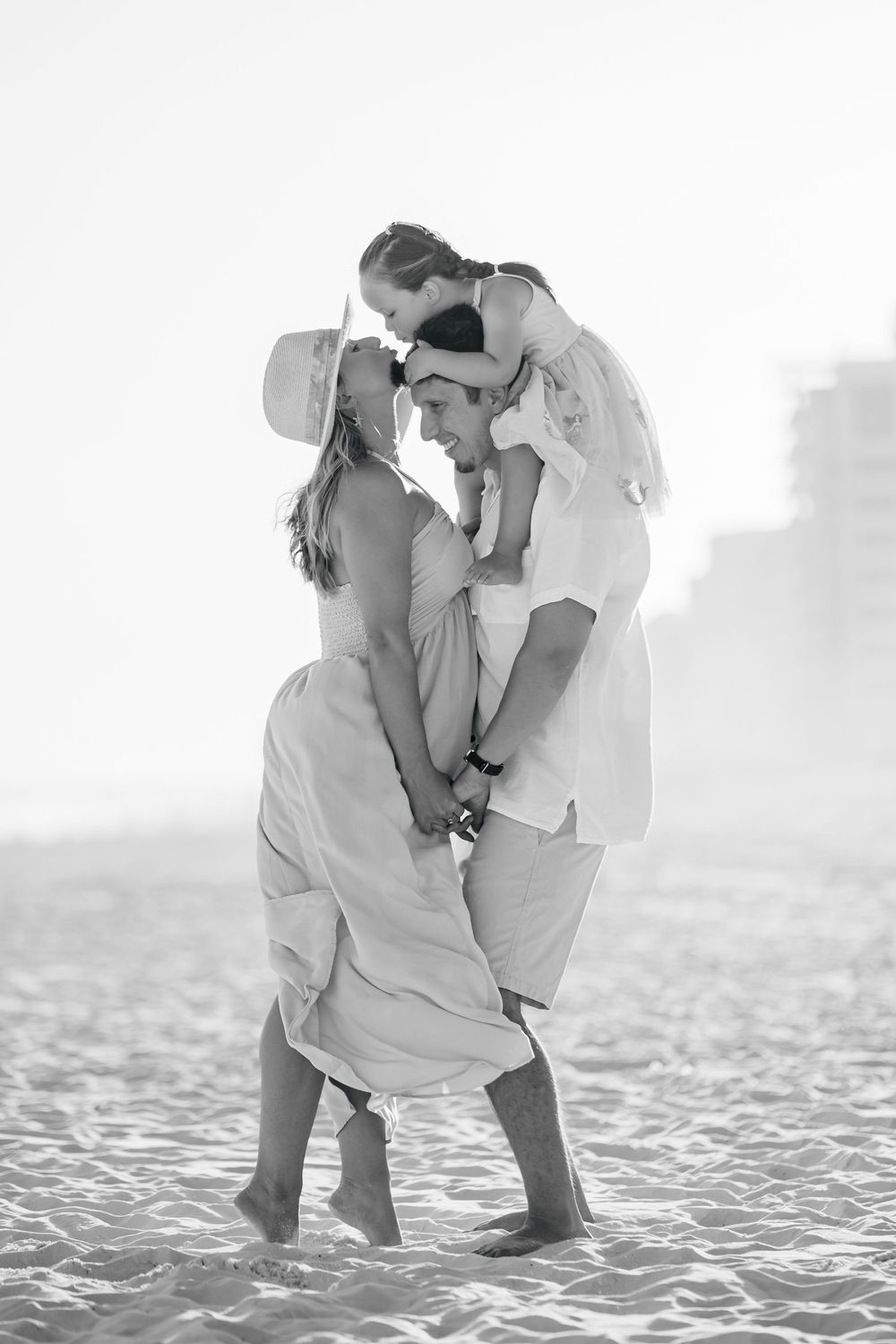 Intimate black and white portrait of family embracing on sandy beach.