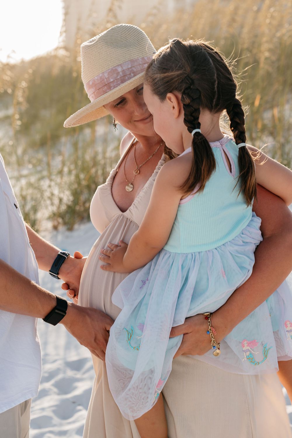 A tender family moment shared on a sunny beach with a little girl in a blue dress.