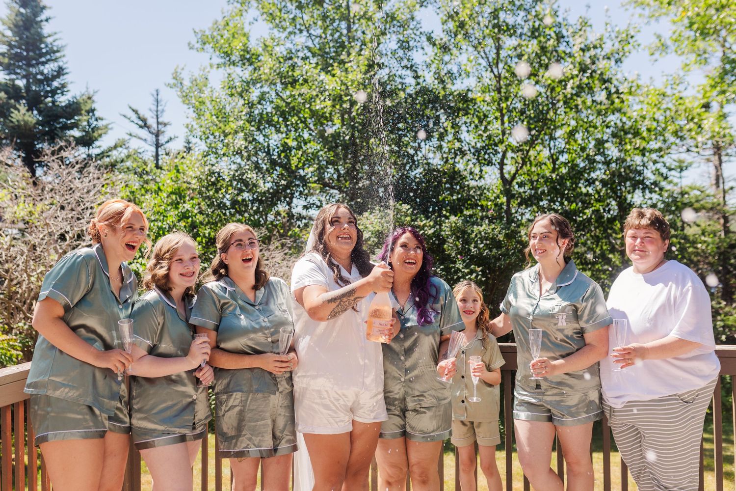 A group in matching khaki uniforms and white shirts standing together on an outdoor wooden deck in bright sunlight.