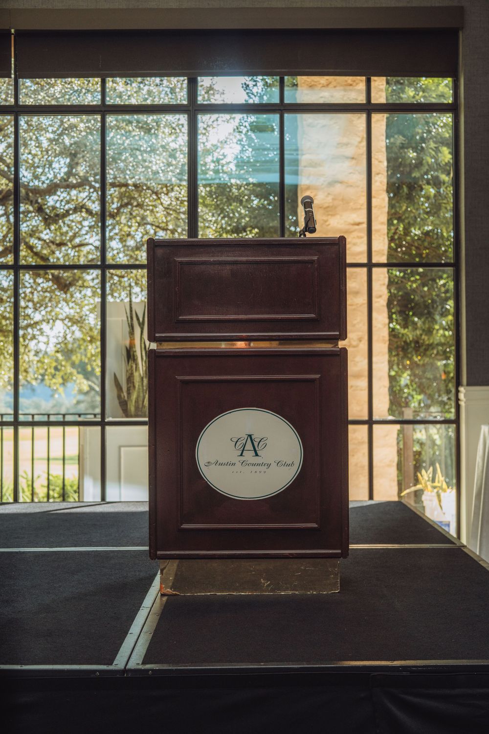 Podium with logo displayed in front of large windows at an event venue.
