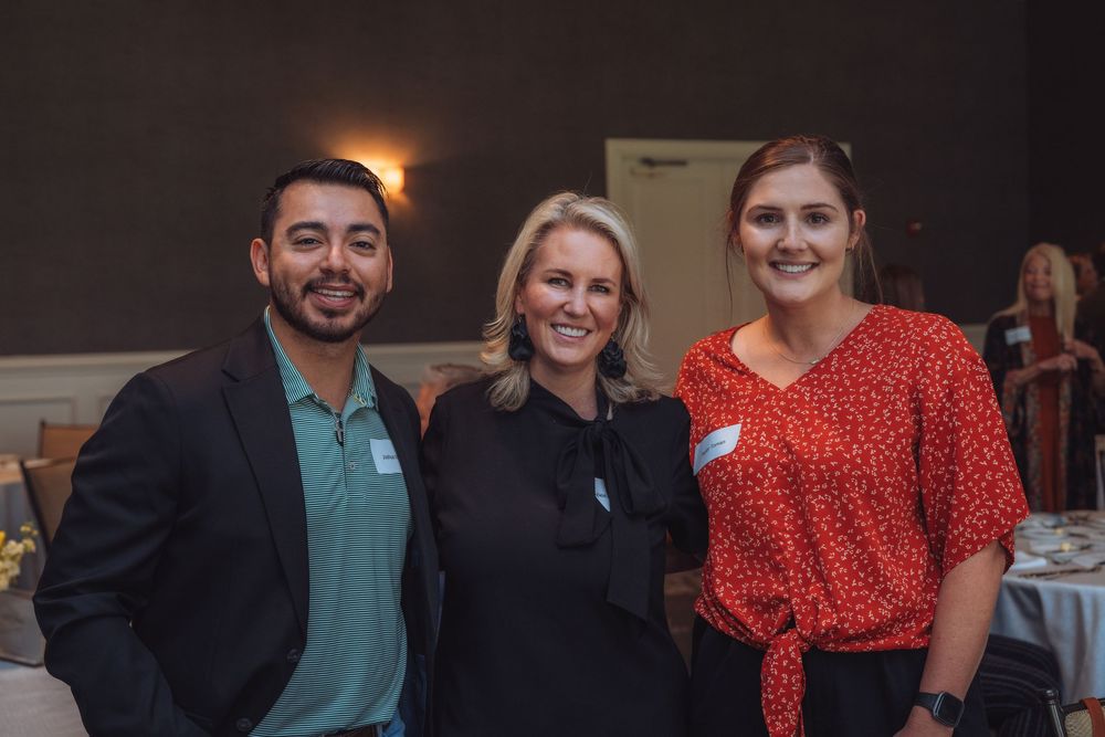 Three professionals networking at a business event in formal attire.