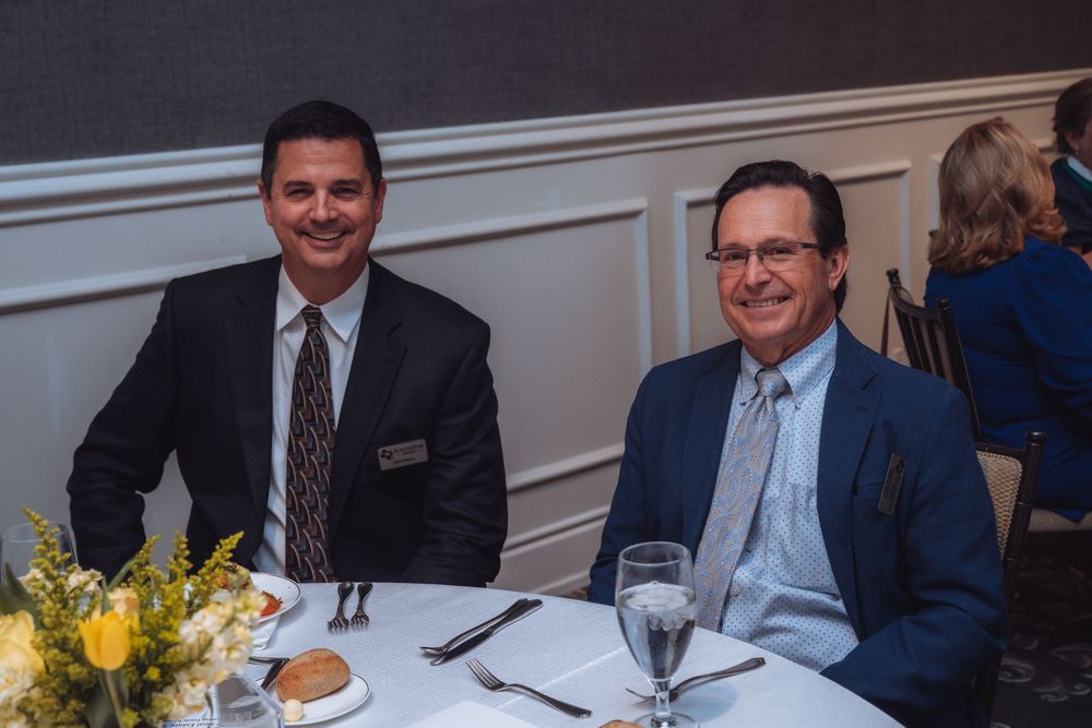 Two business professionals dining at an elegant table with yellow floral centerpiece.