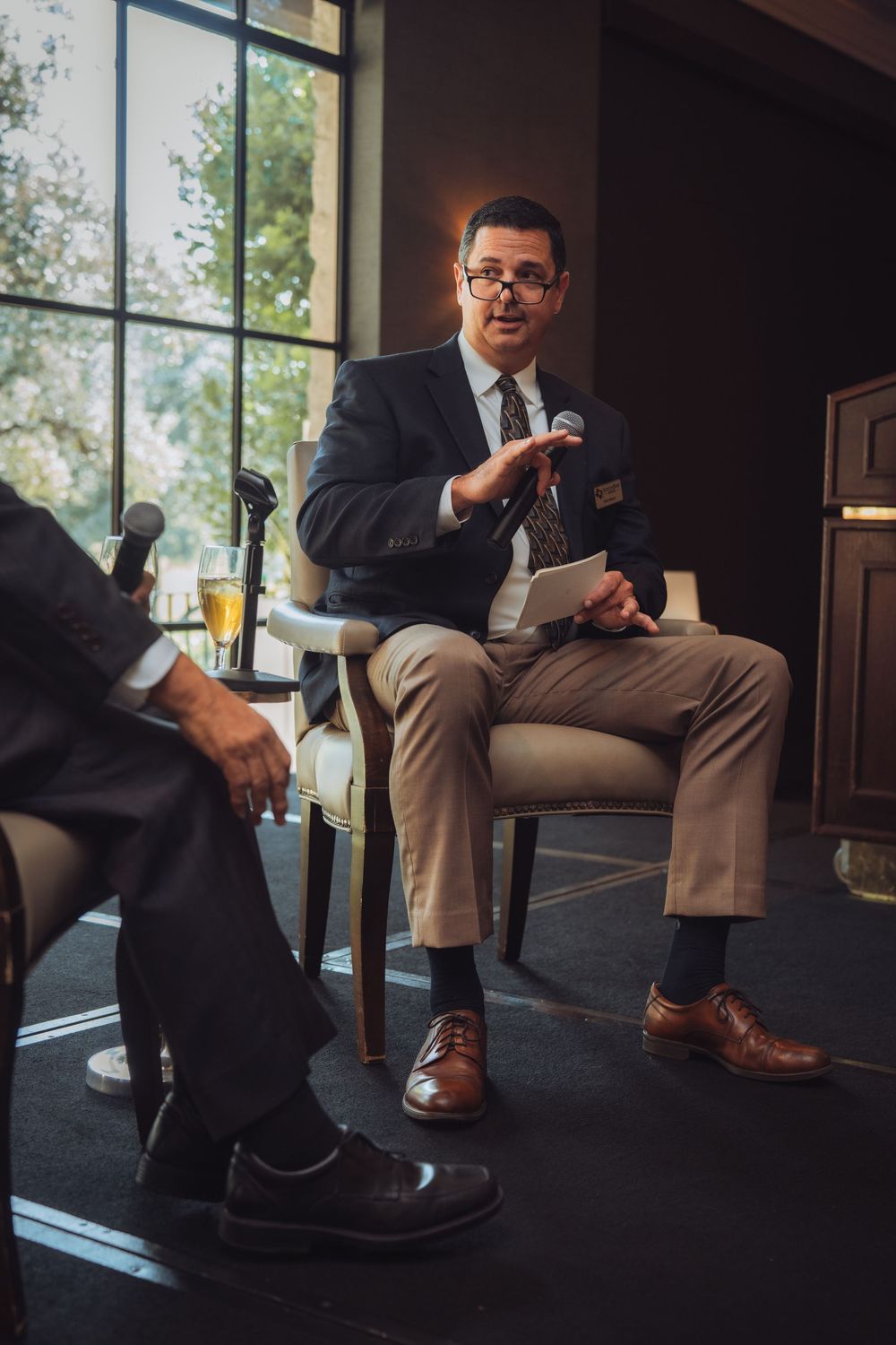Professional speaker gesturing while seated during business presentation.
