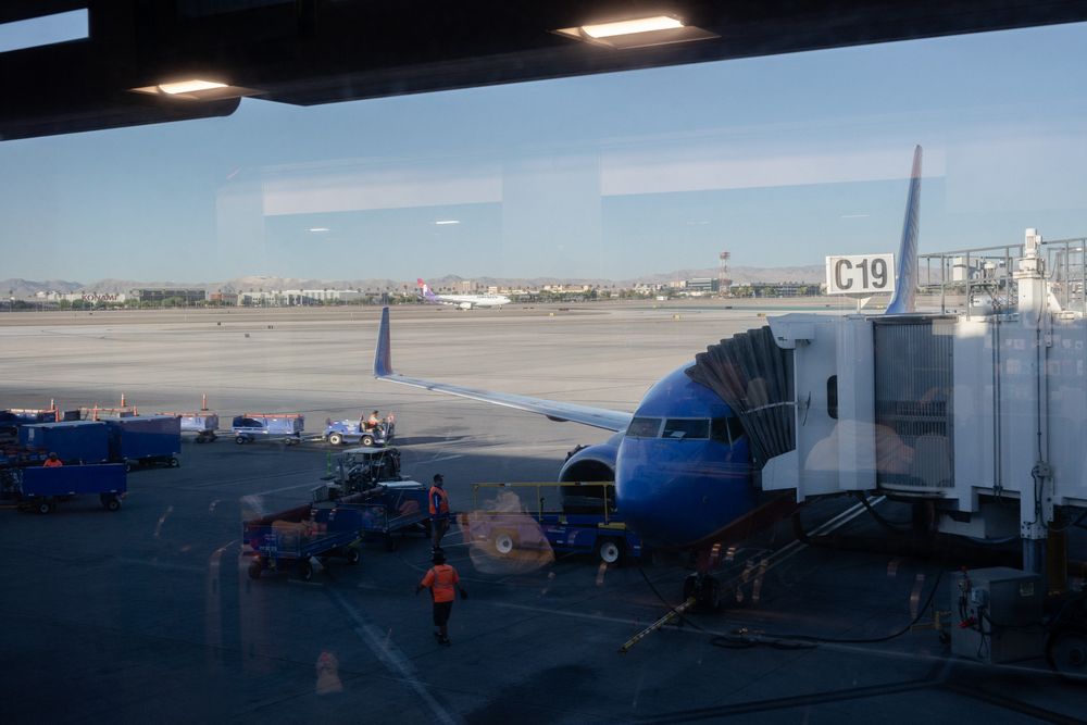 Airport tarmac with parked aircraft and terminal buildings under blue skies.
