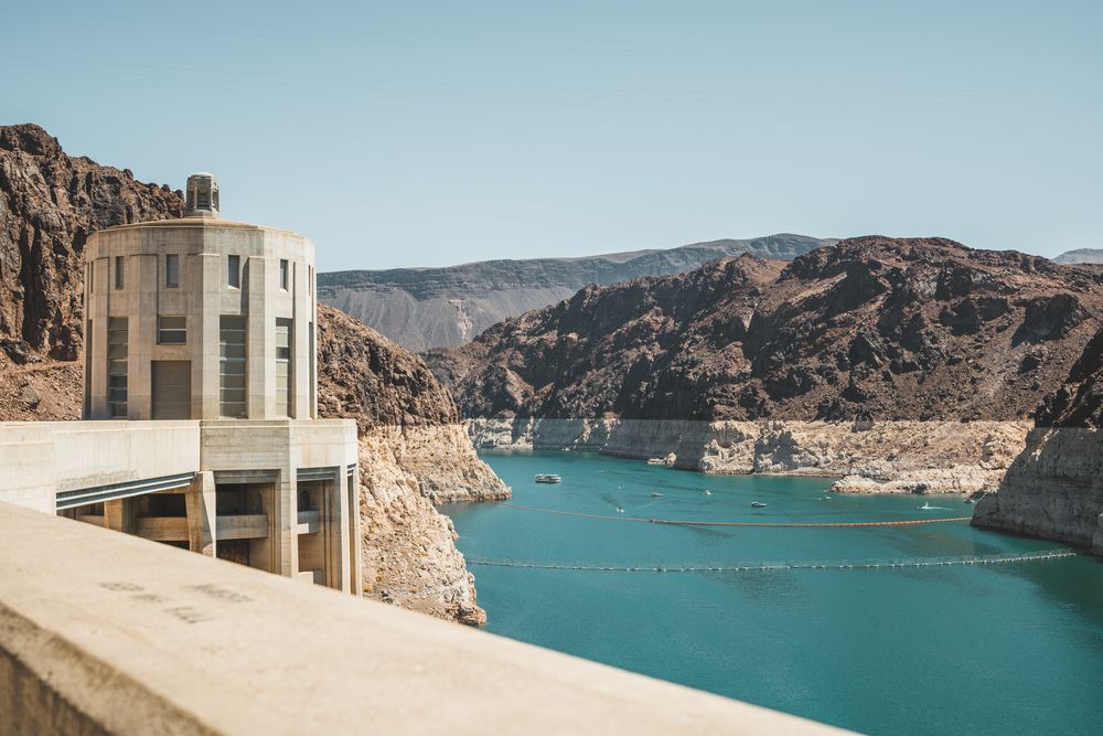 Art deco style dam building overlooking bright blue reservoir waters surrounded by desert cliffs.