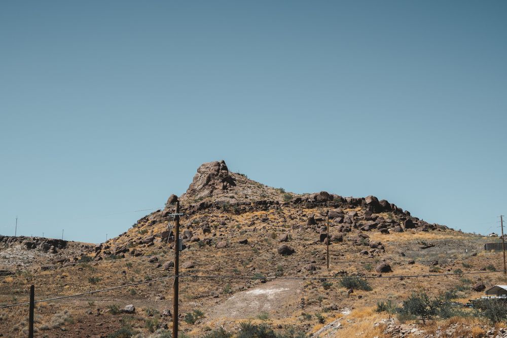 Rocky desert hill with transmission poles against bright blue sky.