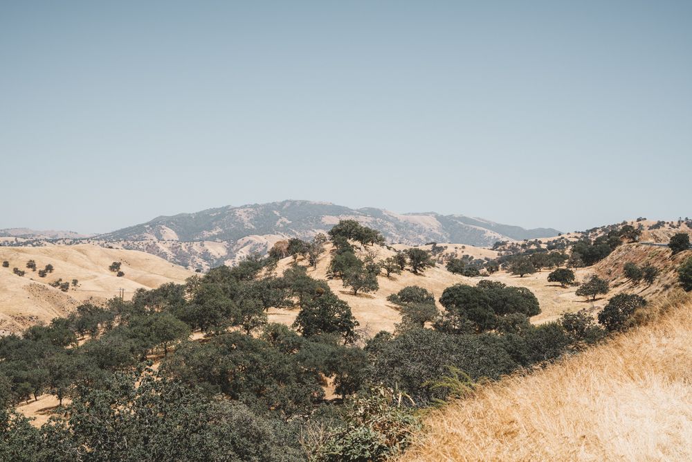 Rolling golden hills and mountains stretch across a scenic California landscape under blue skies.